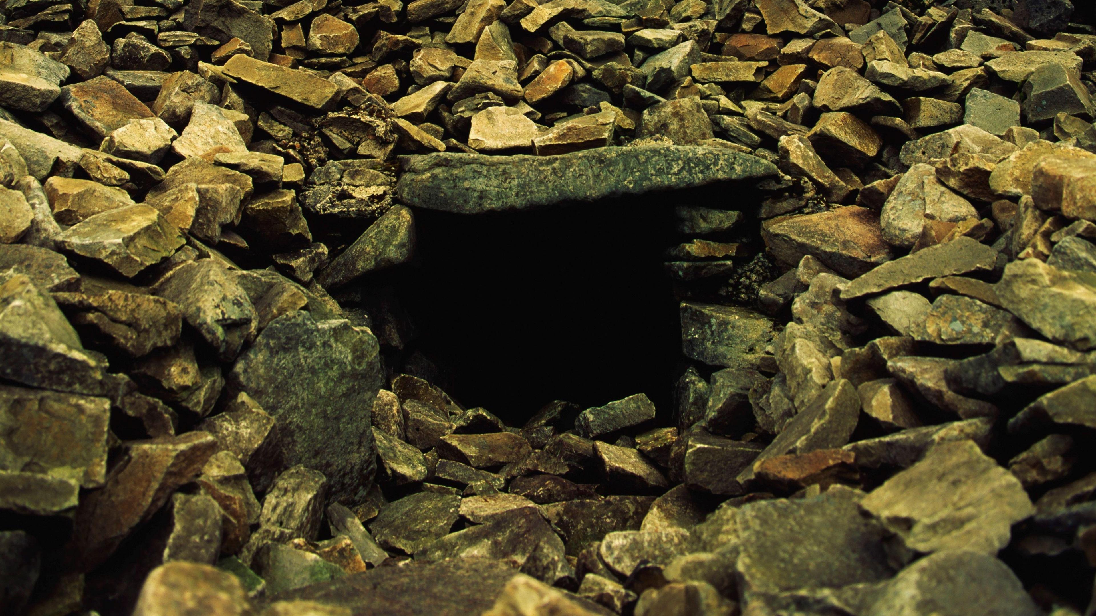 Cailleach Beara's House on the summit Of Slieve Gullion shows a passageway held up by slabs of stone that are surrounded by grey rocks.