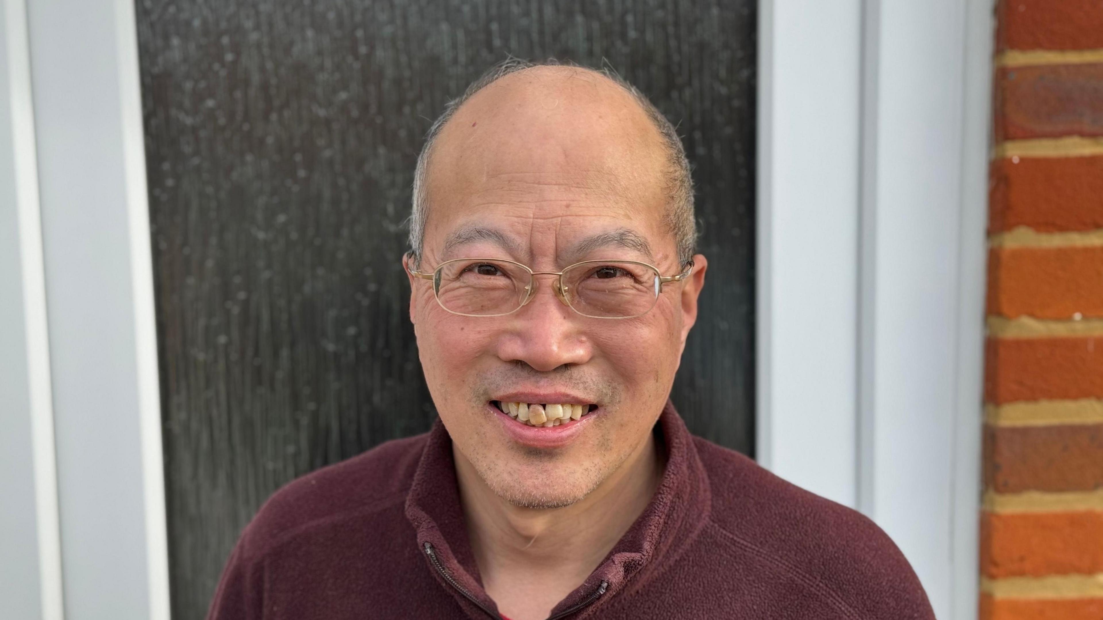 Wenge Yuan standing in front of his front door while smiling into the camera