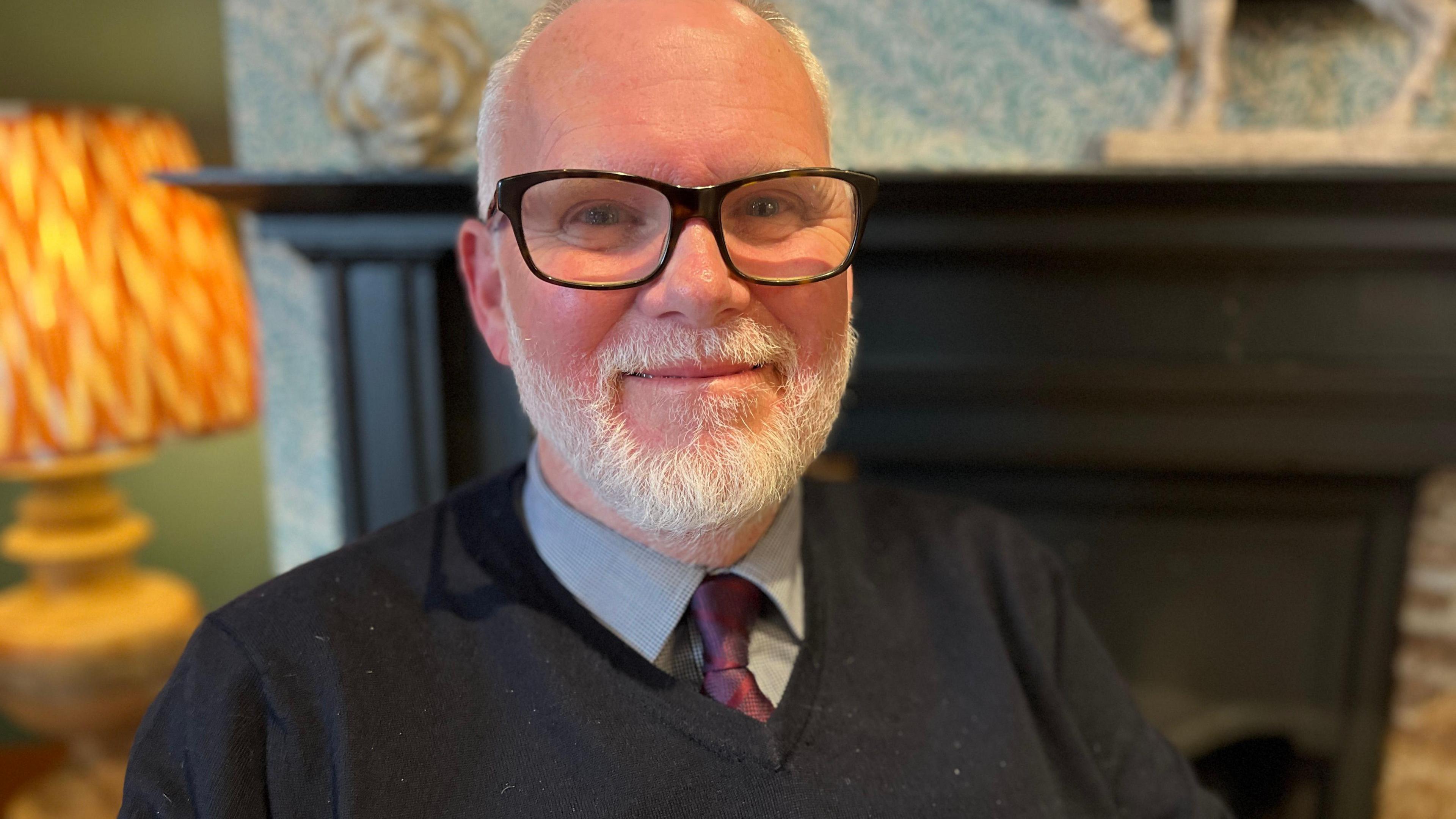 Alan Hagger smiles in front of fireplace