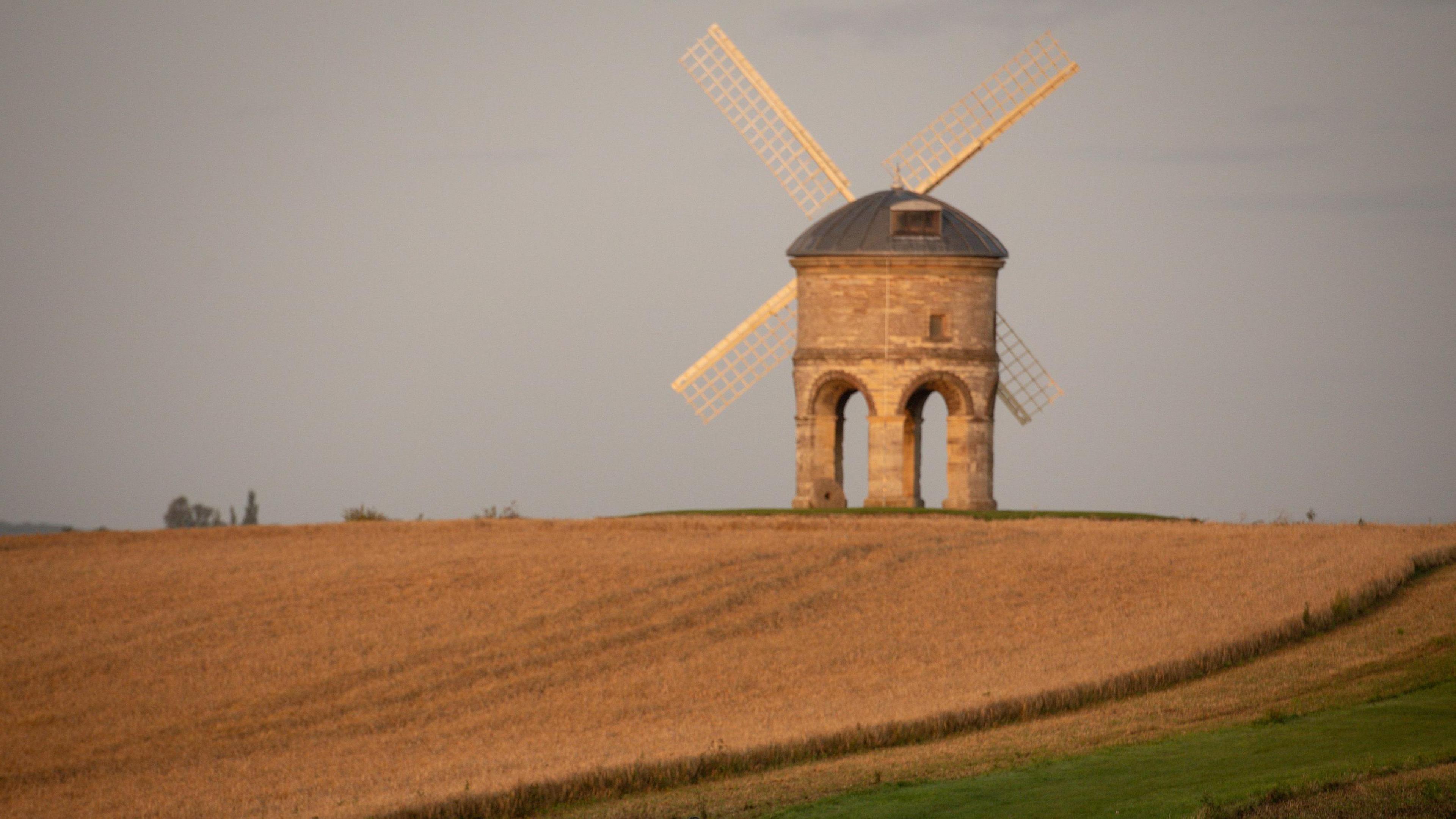 A windmill on a hilltop, with circular stone arches supporting a round tower, with metal dome roof. 