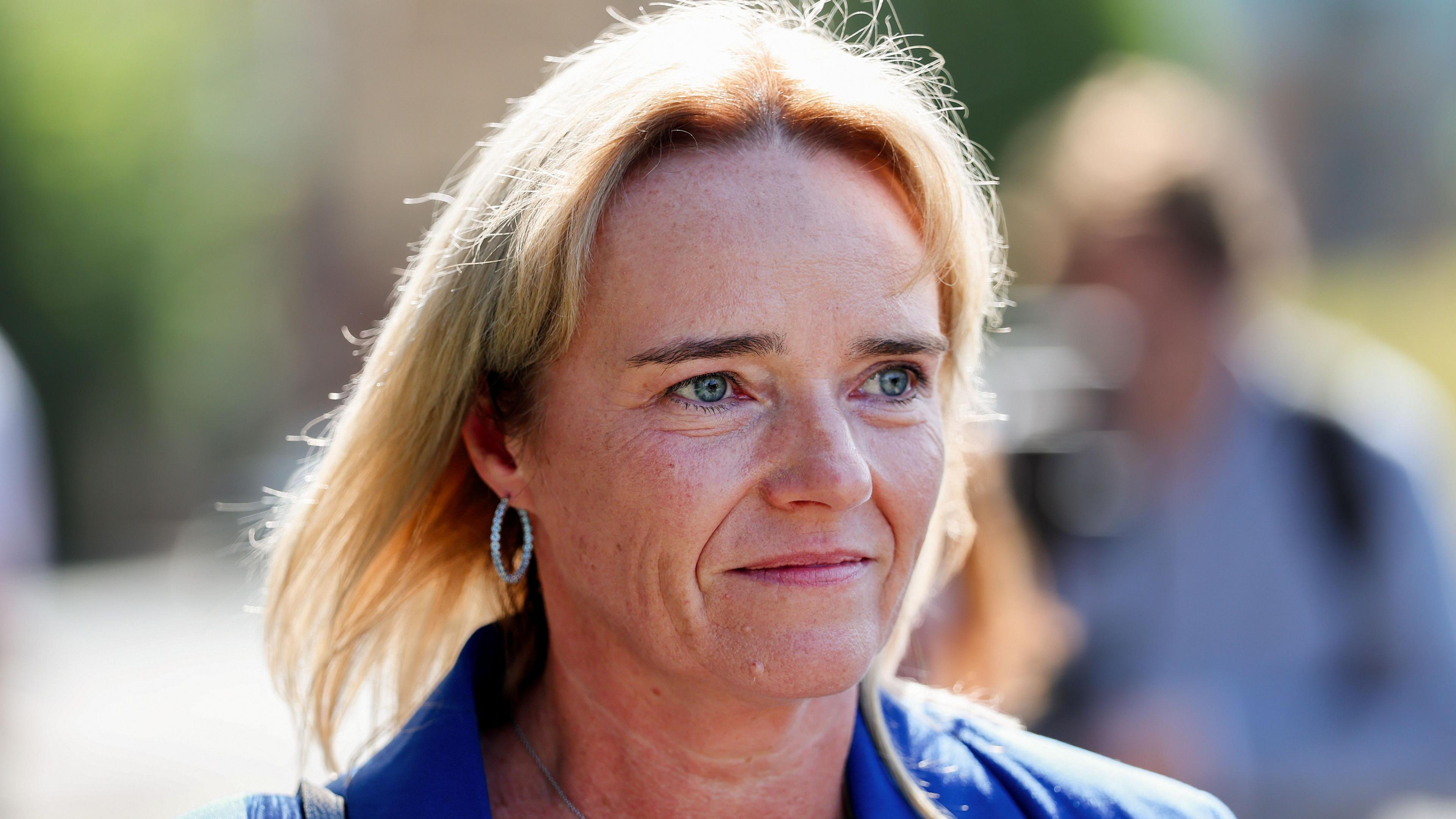 Sandie Peggie departing the tribunal. She has shoulder-length, blonde hair and is wearing a blue jacket and hoop earrings.