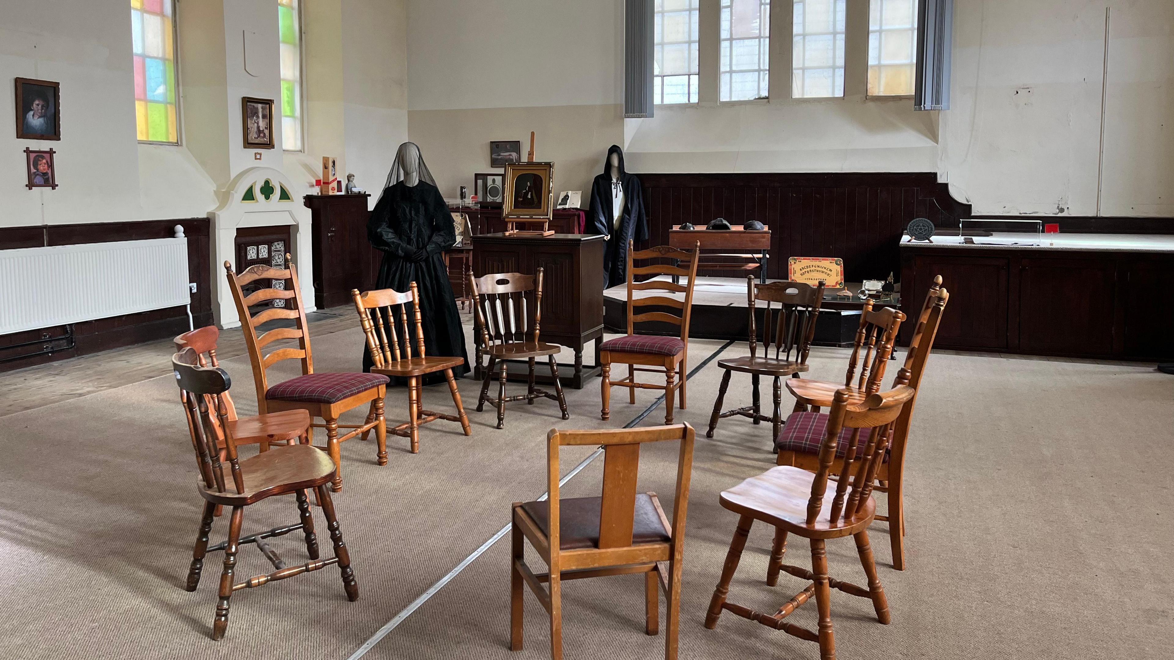 Chairs in a circle and mannequins wearing black dress and cloak and veil in the background