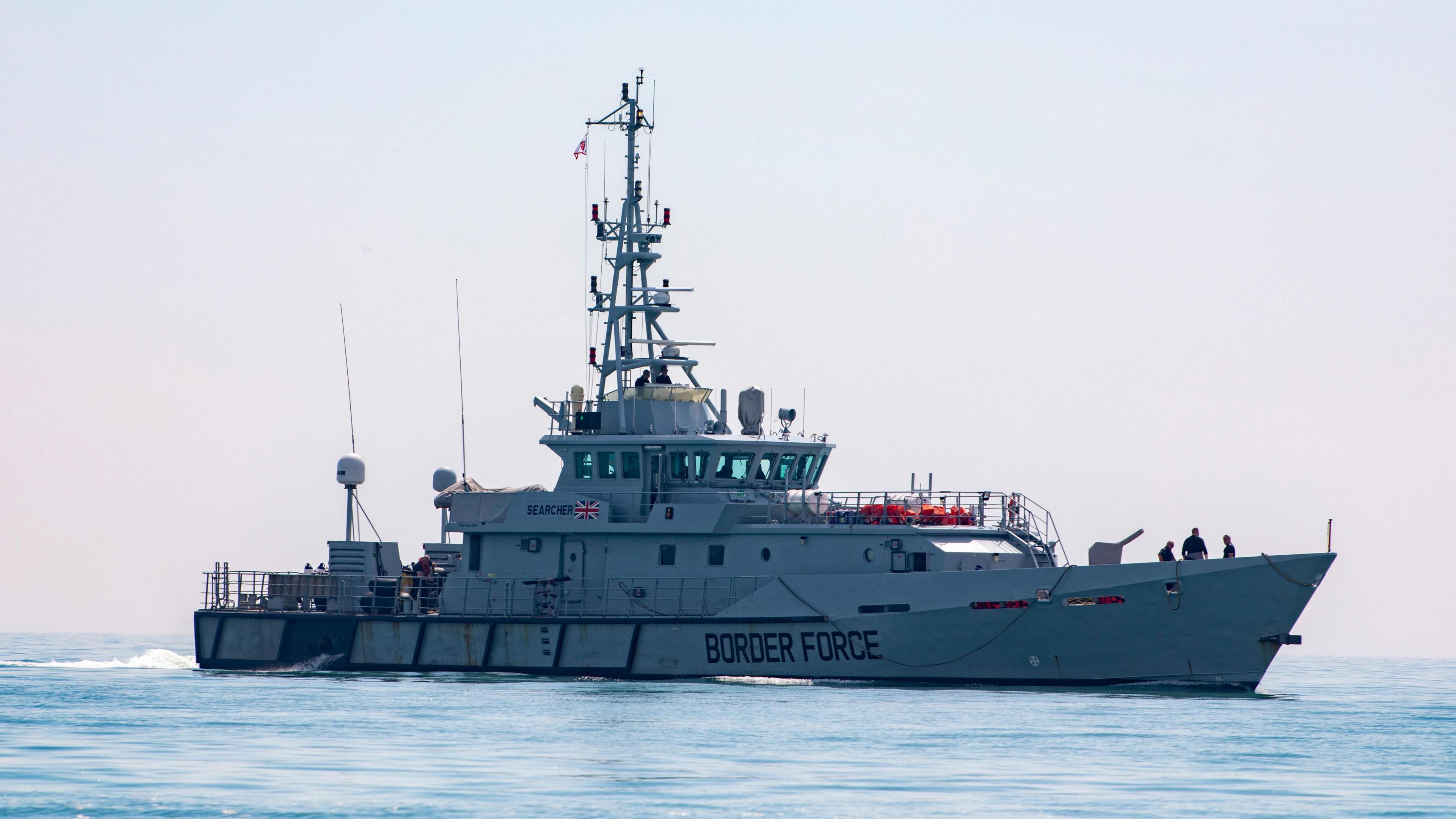 A grey boat in a body of water. There is a Great Britain flag on the side along with "BORDER FORCE" in text.