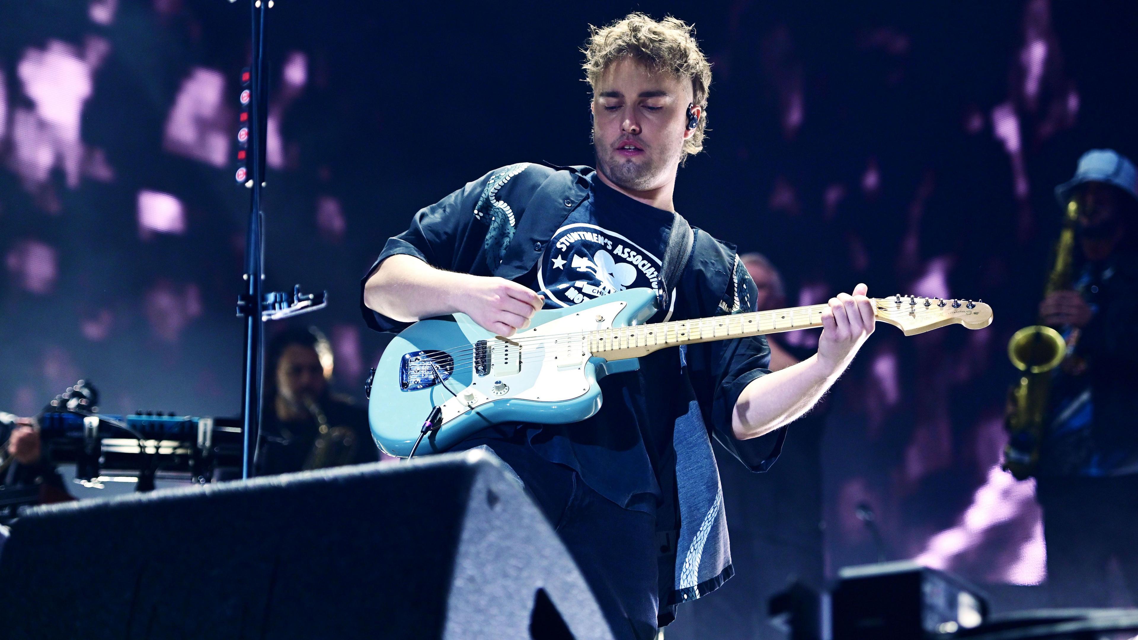 Sam Fender performing on stage, holding a baby blue electric guitar. 