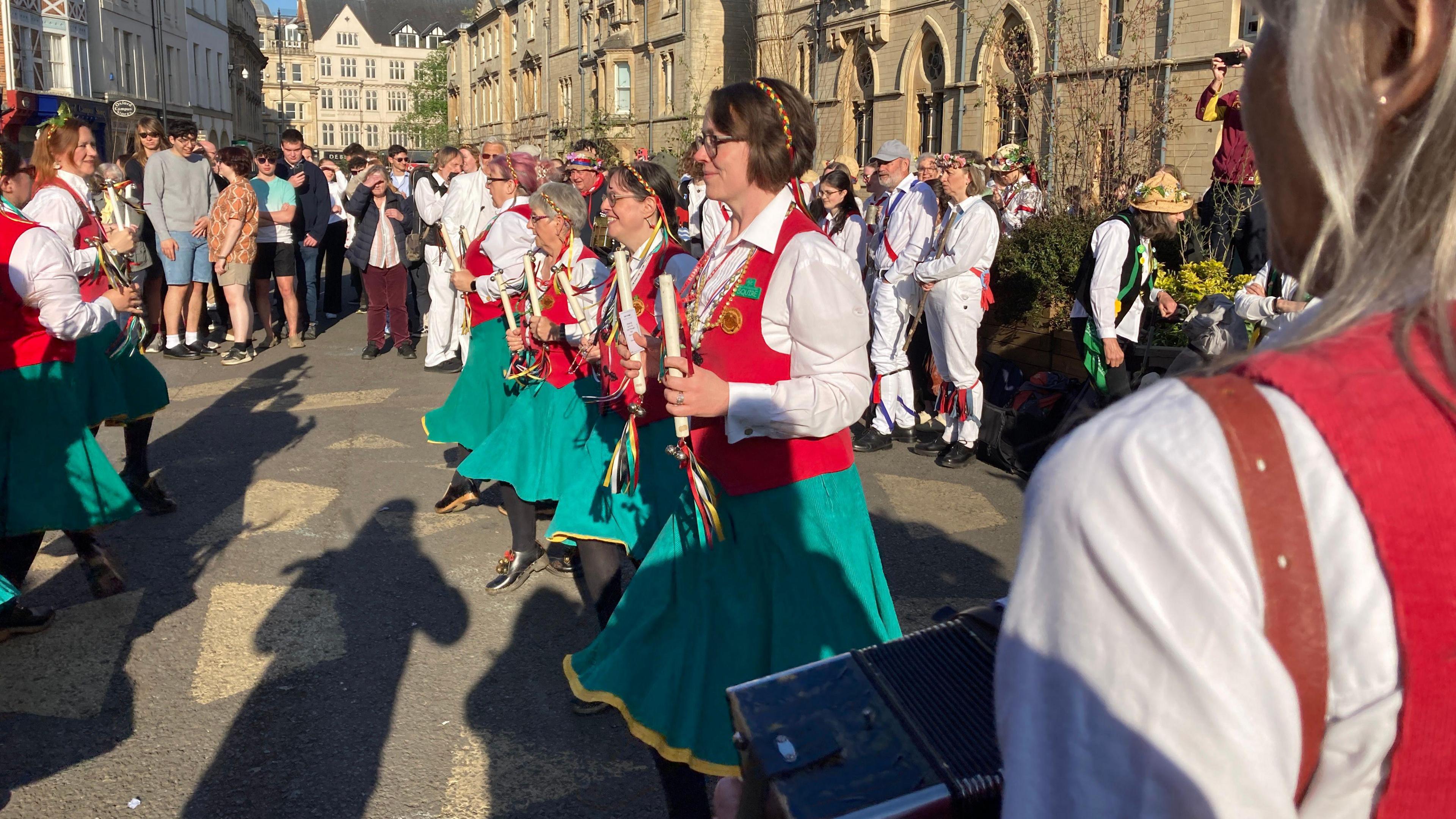 A group of women in green skirts and red waistcoats dancing in unison