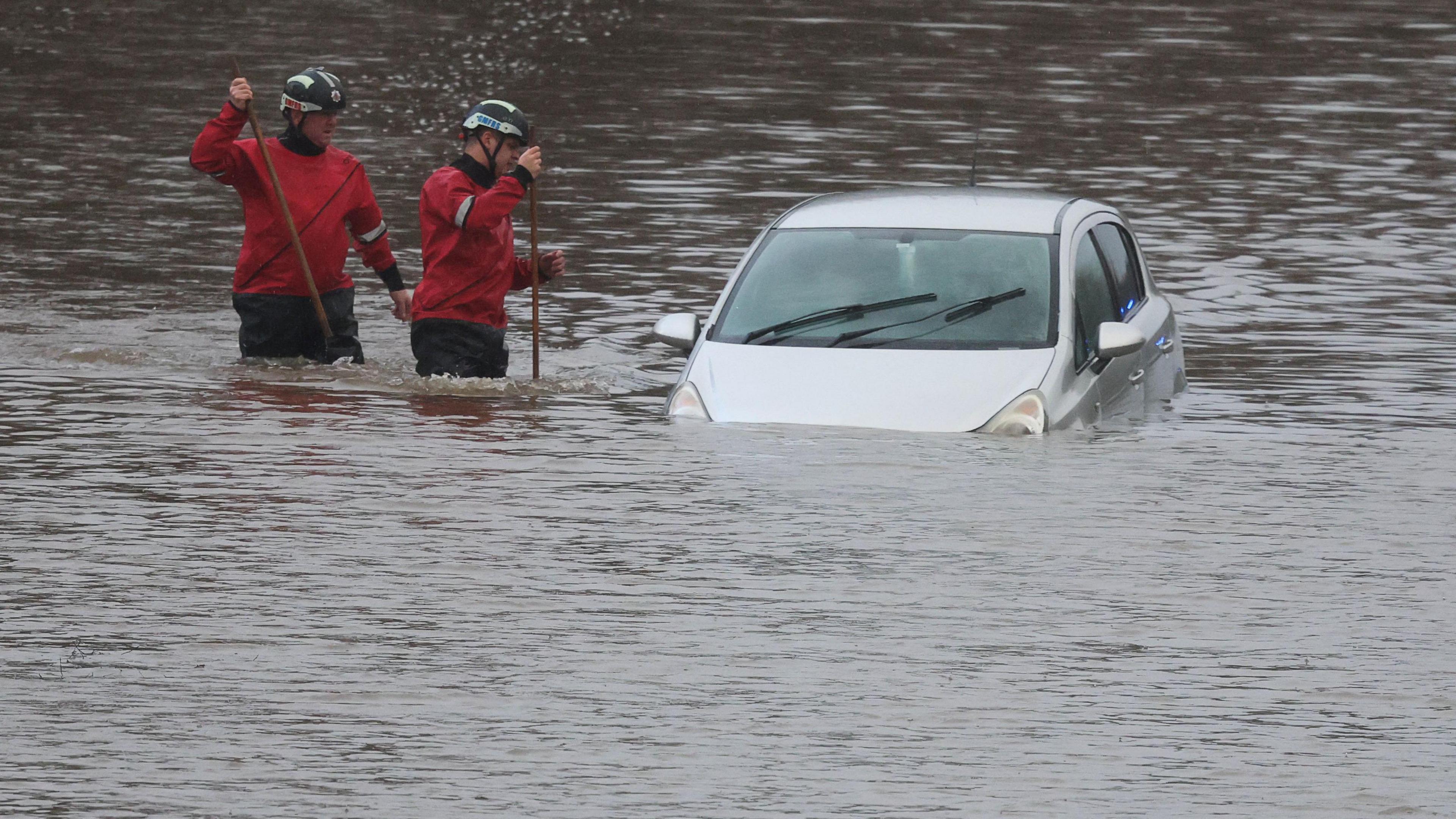 firefighters helping a man stuck in his care in the floods.