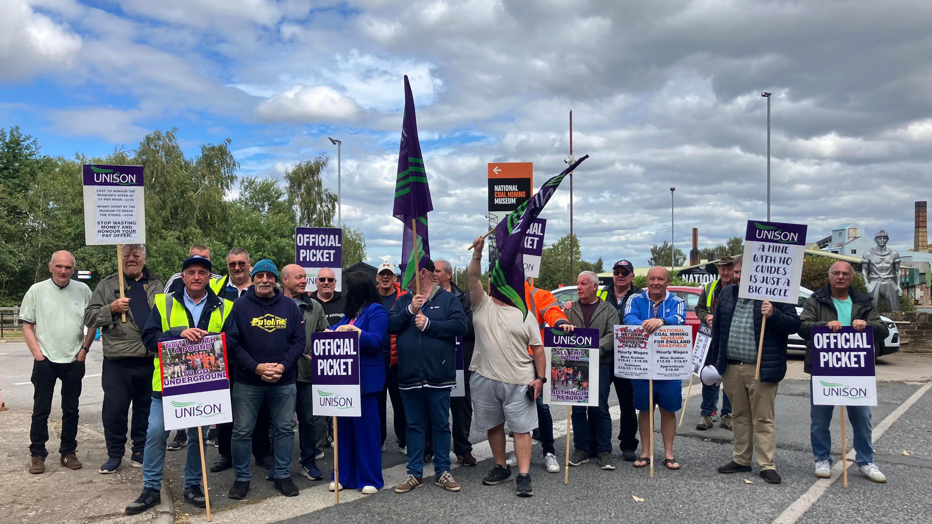 A group of striking workers on a picket line. Most are holding up placards reading 'official picket'.