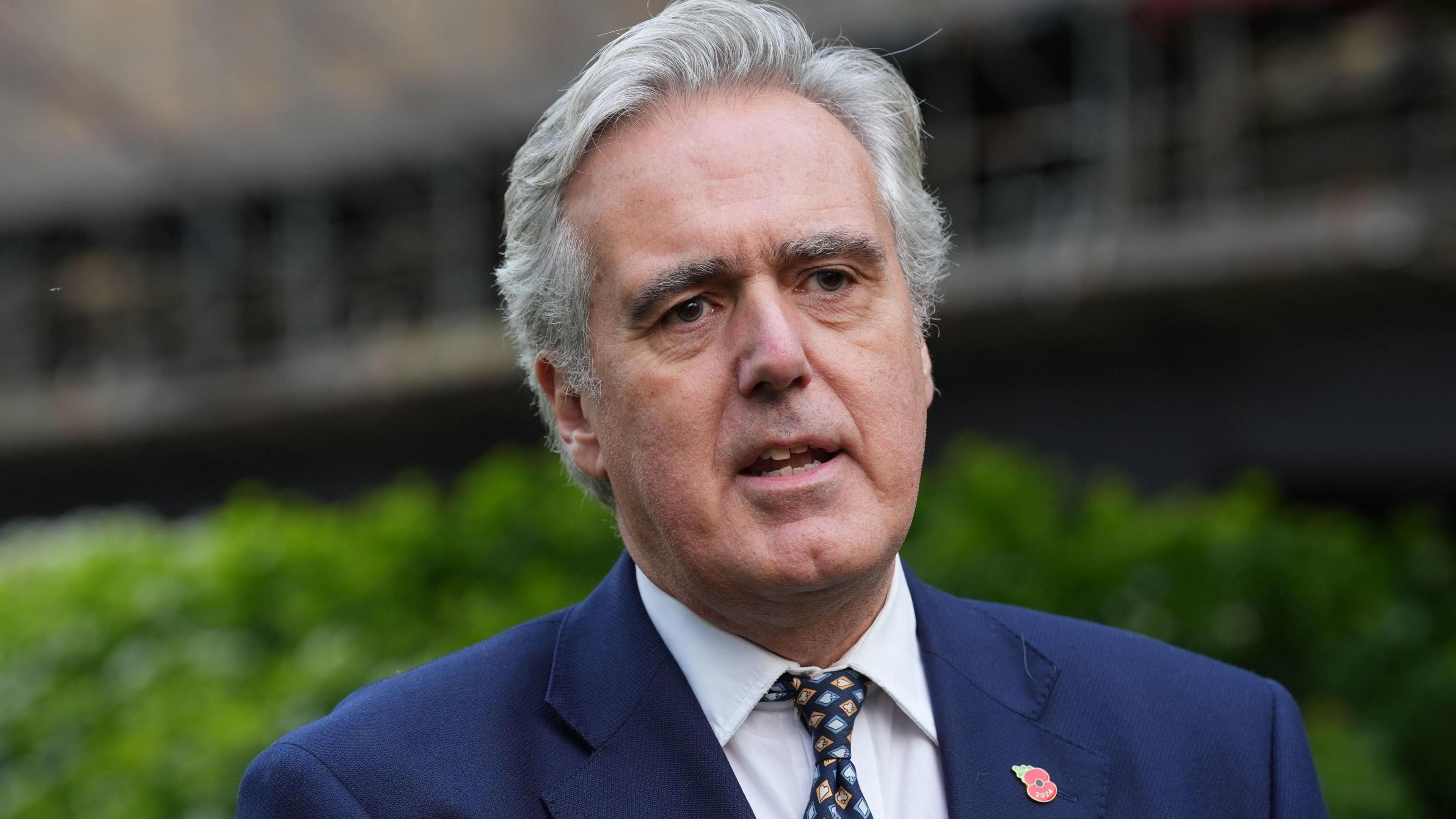 A man with grey hair wearing a blue suit, white shirt and patterned tie