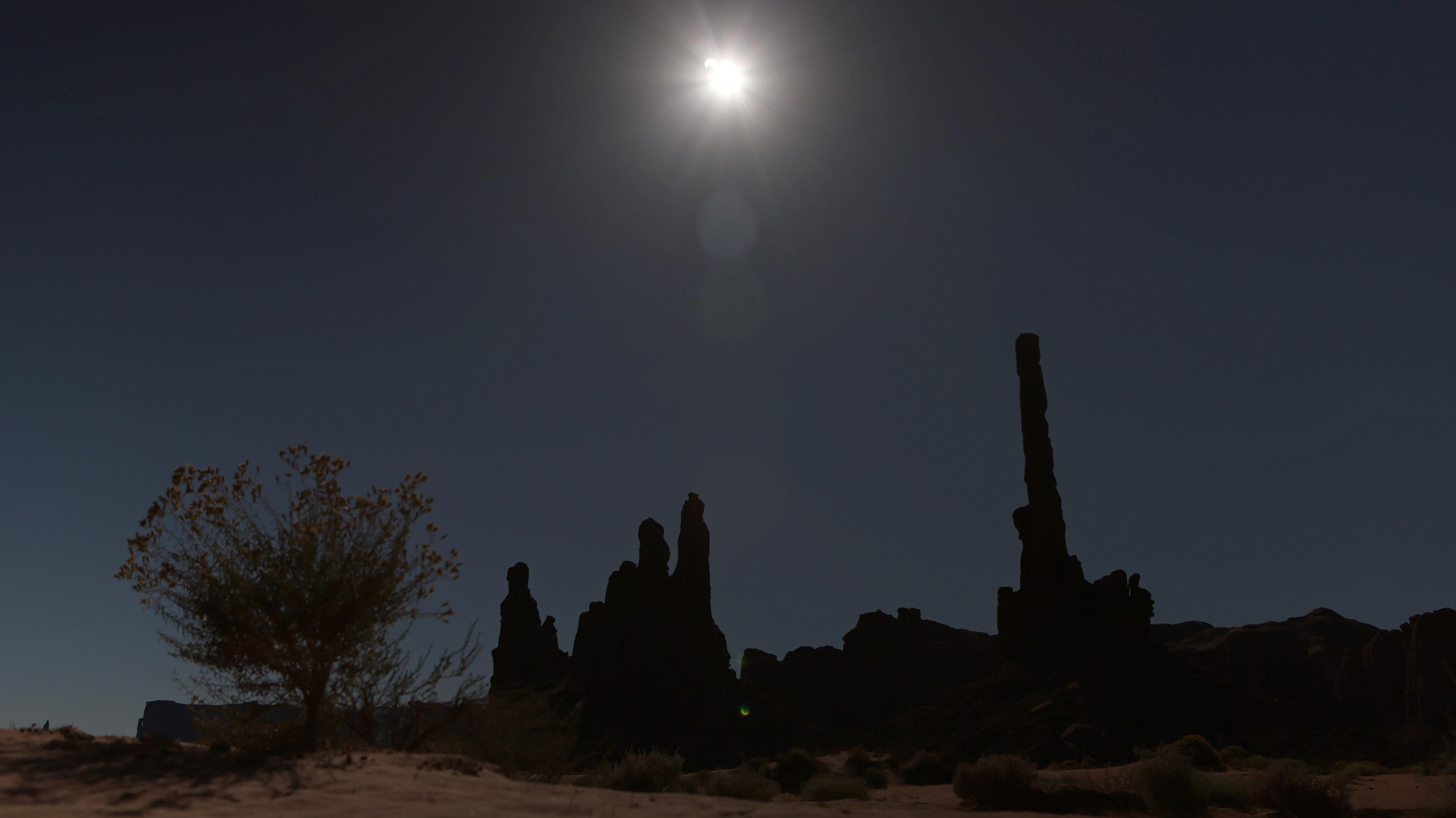 A dark sky over silhouetted desk rocks under a partially obscured Sun