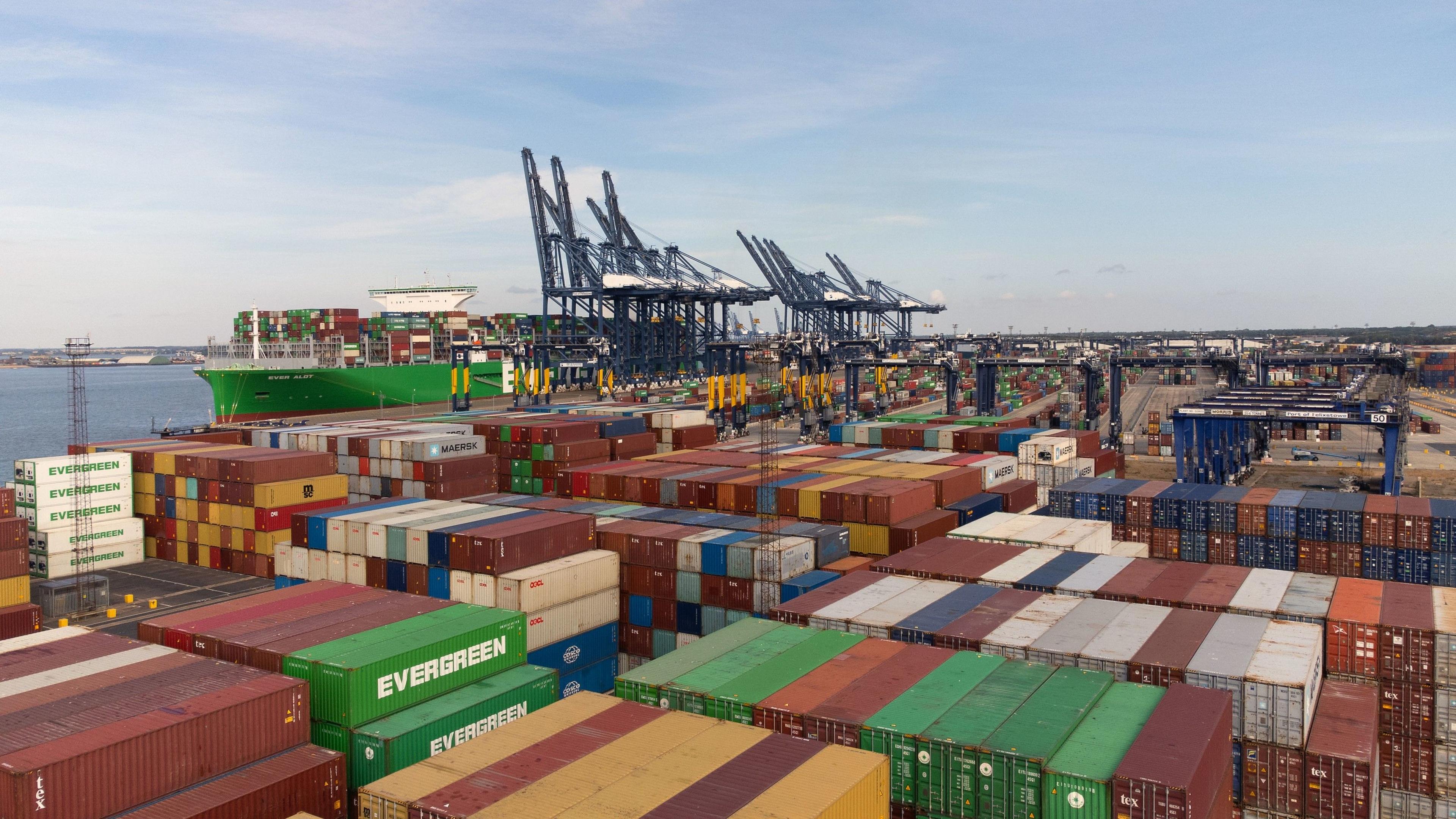 A drone image of the Port of Felixstowe. Shipping containers are stacked on top of each other while a green ship and several cranes are in the distance.