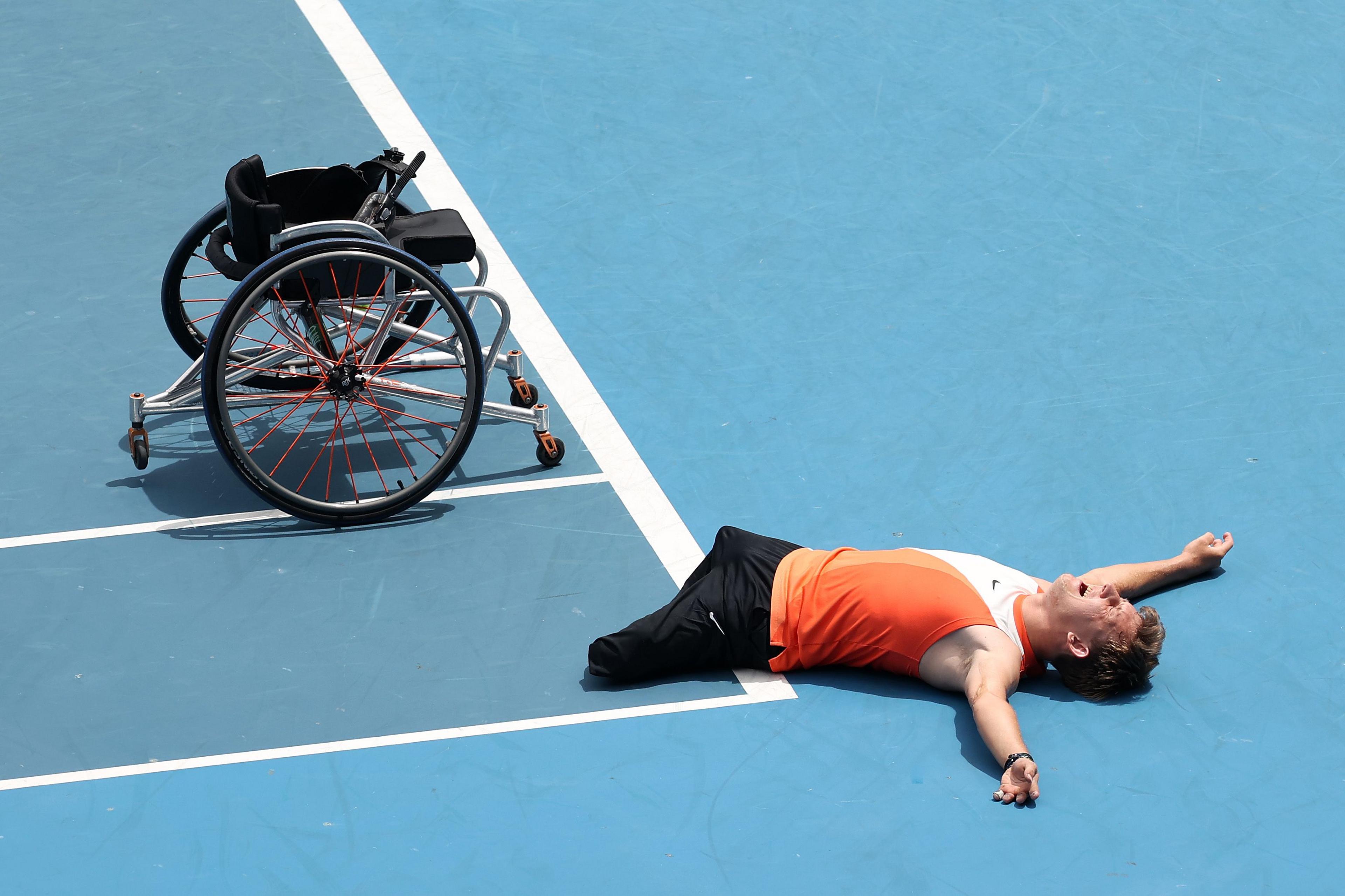 Wheelchair athlete Niels Vink lies flat on a blue court beside his wheelchair, arms outstretched, in celebration after winning the Quad Wheelchair Singles Final at the Australian Open, Melbourne Park. 