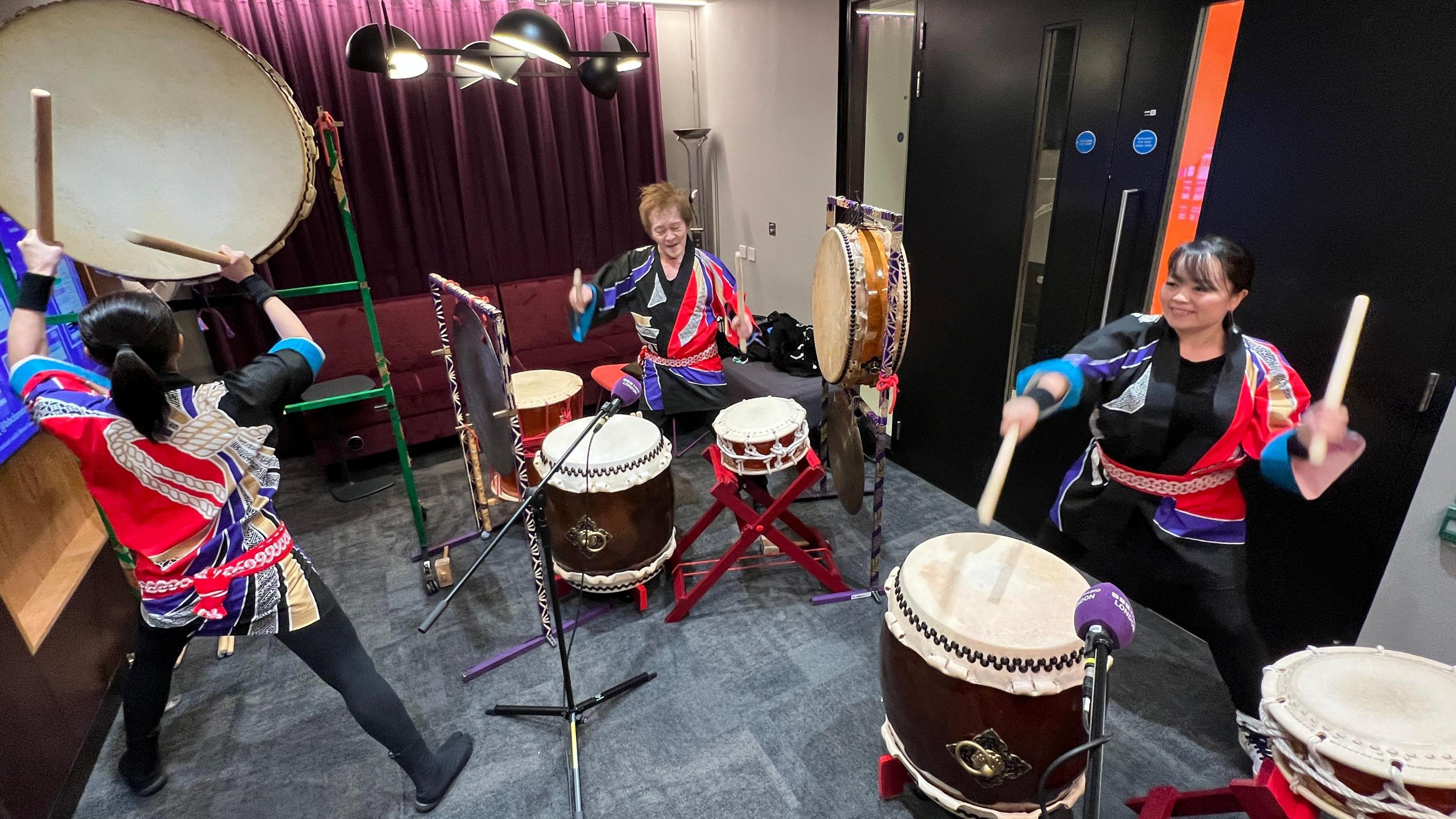 Three musicians are drumming inside the BBC London office.