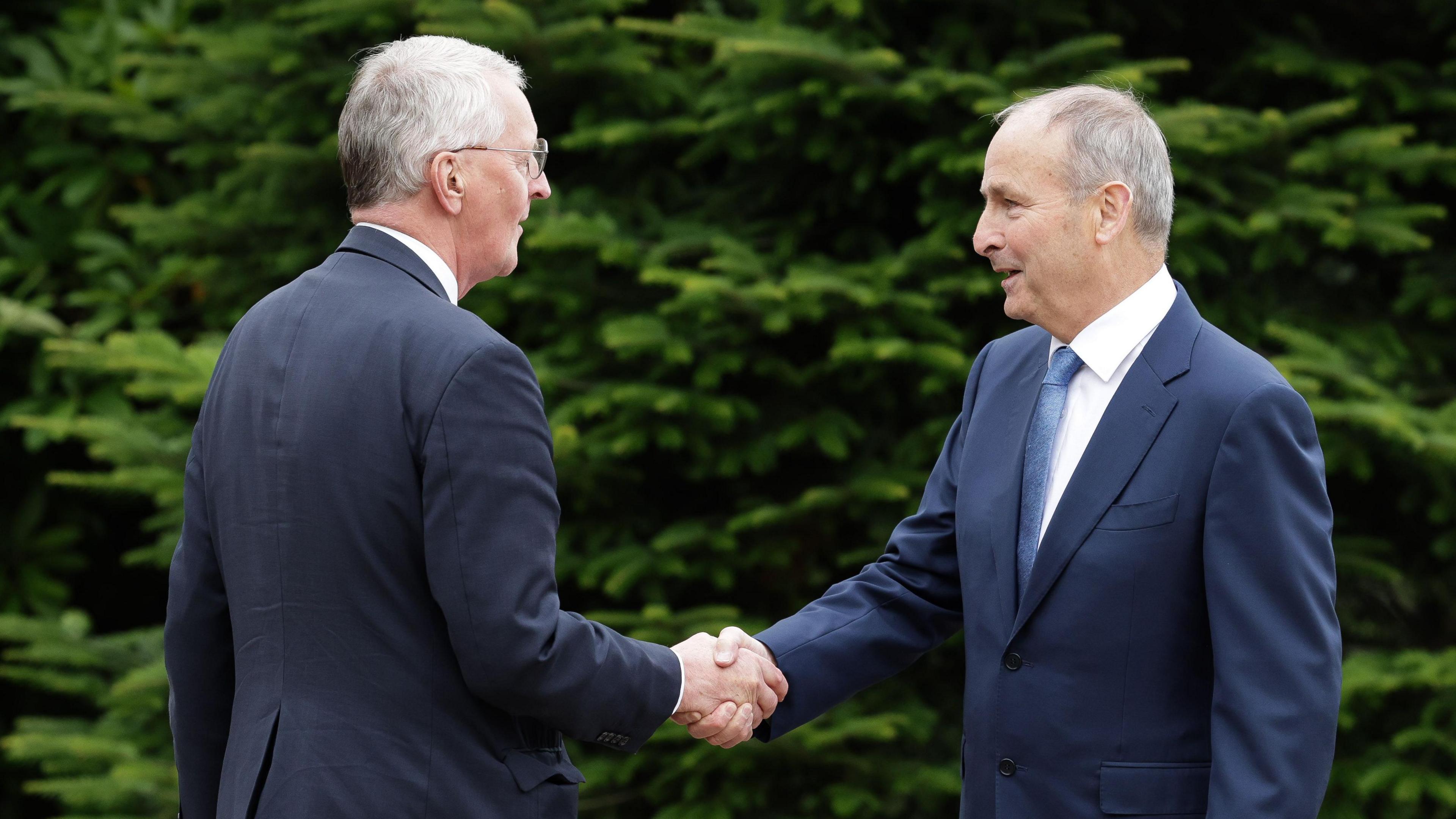 Hilary Benn and Micheál Martin shaking hands in front of greenery at Hillsborough