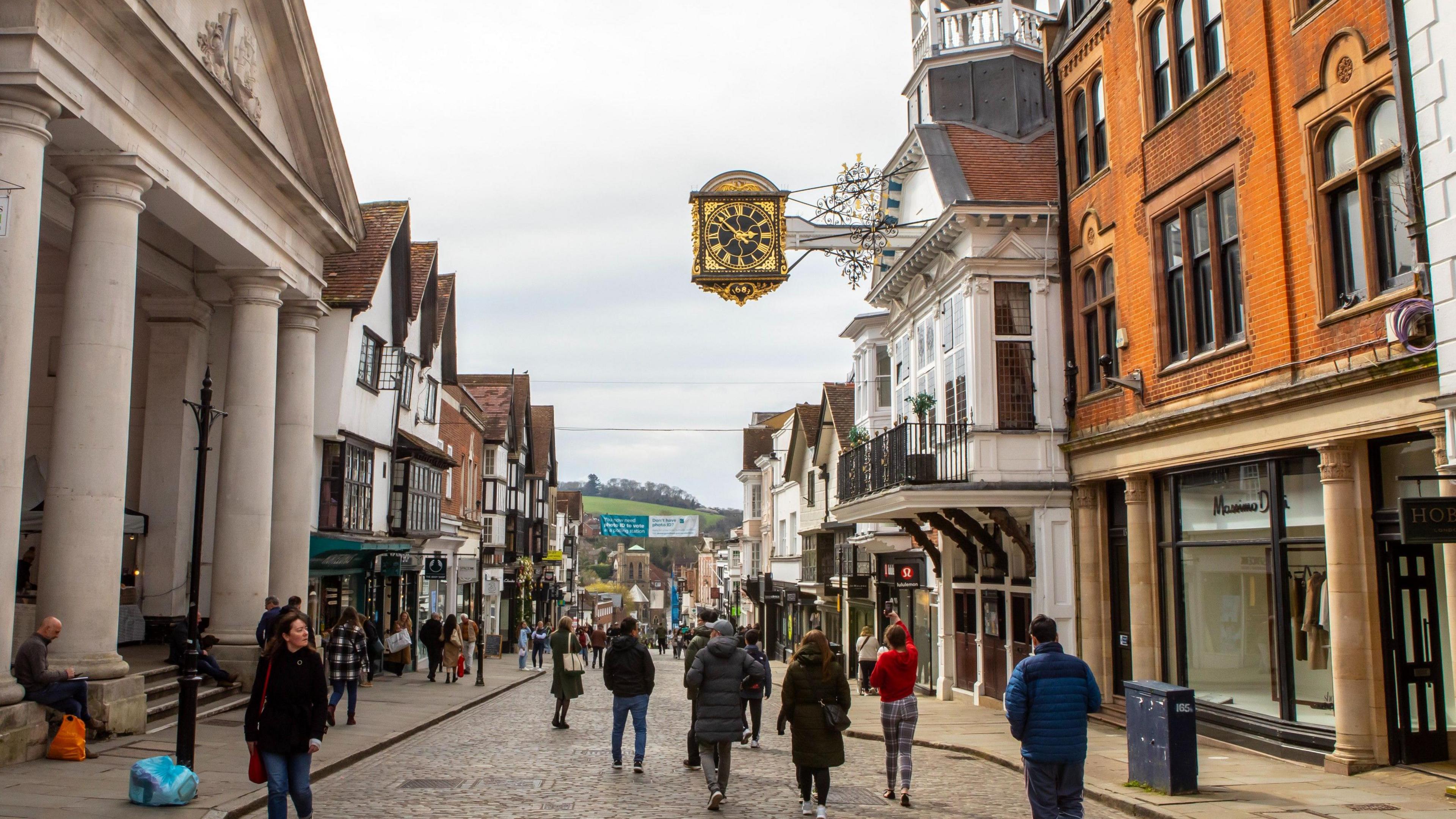 Guildford High Street, with the clock tower in the foreground and shoppers using the pedestrianised area.