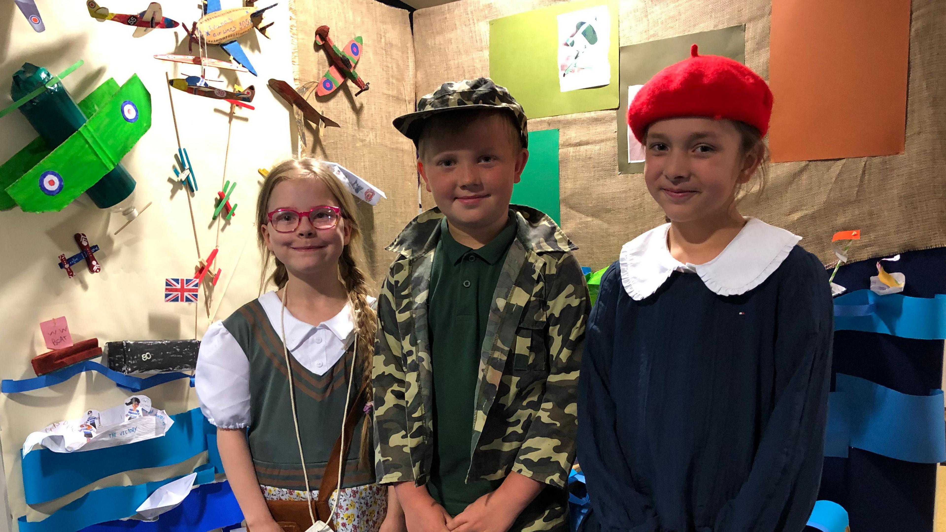 Evie, Max and Milly dressed in 1940s style clothing in front of a display of D-Day vehicles