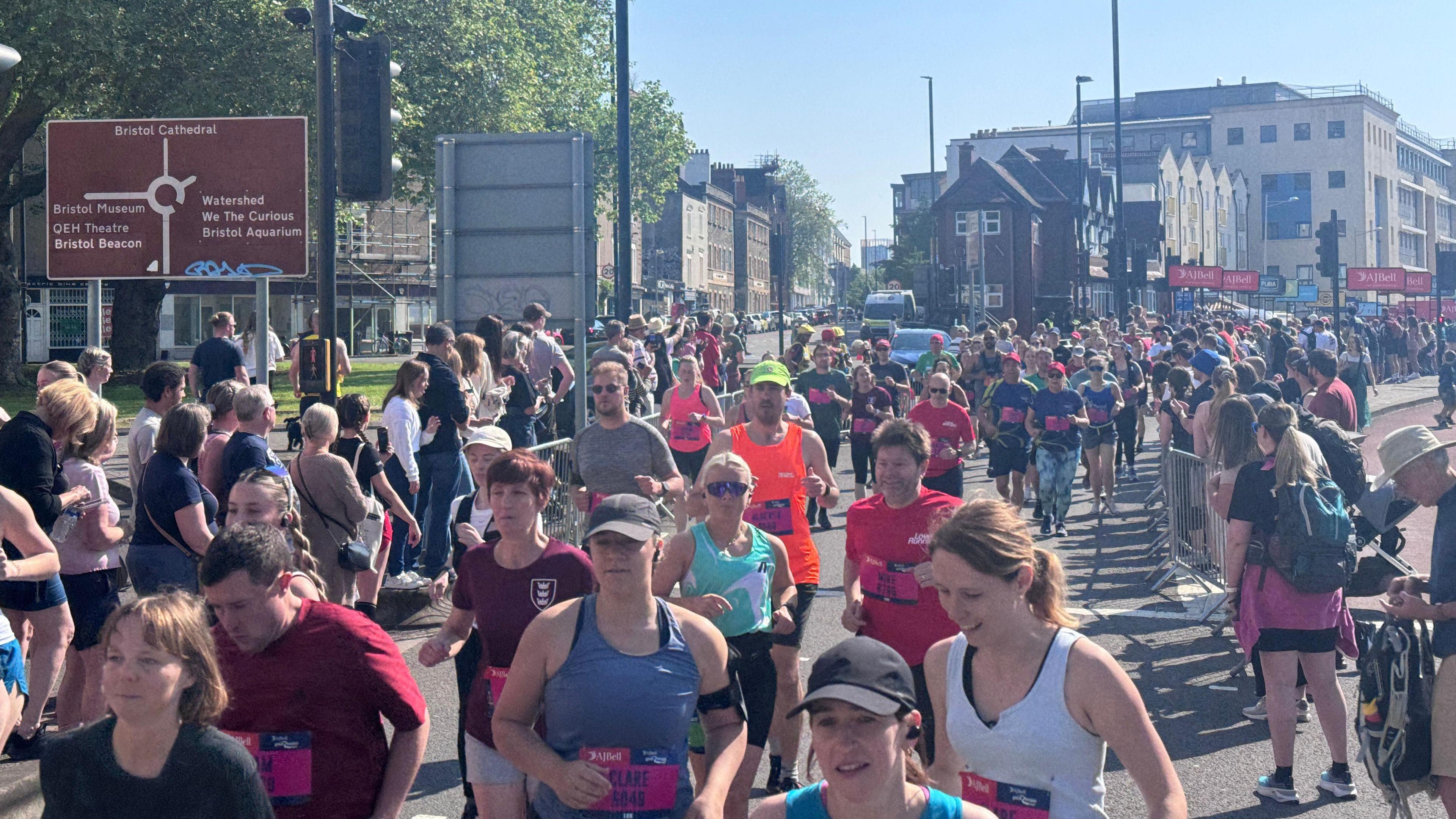 People running down the road while spectators watch from behind the partition