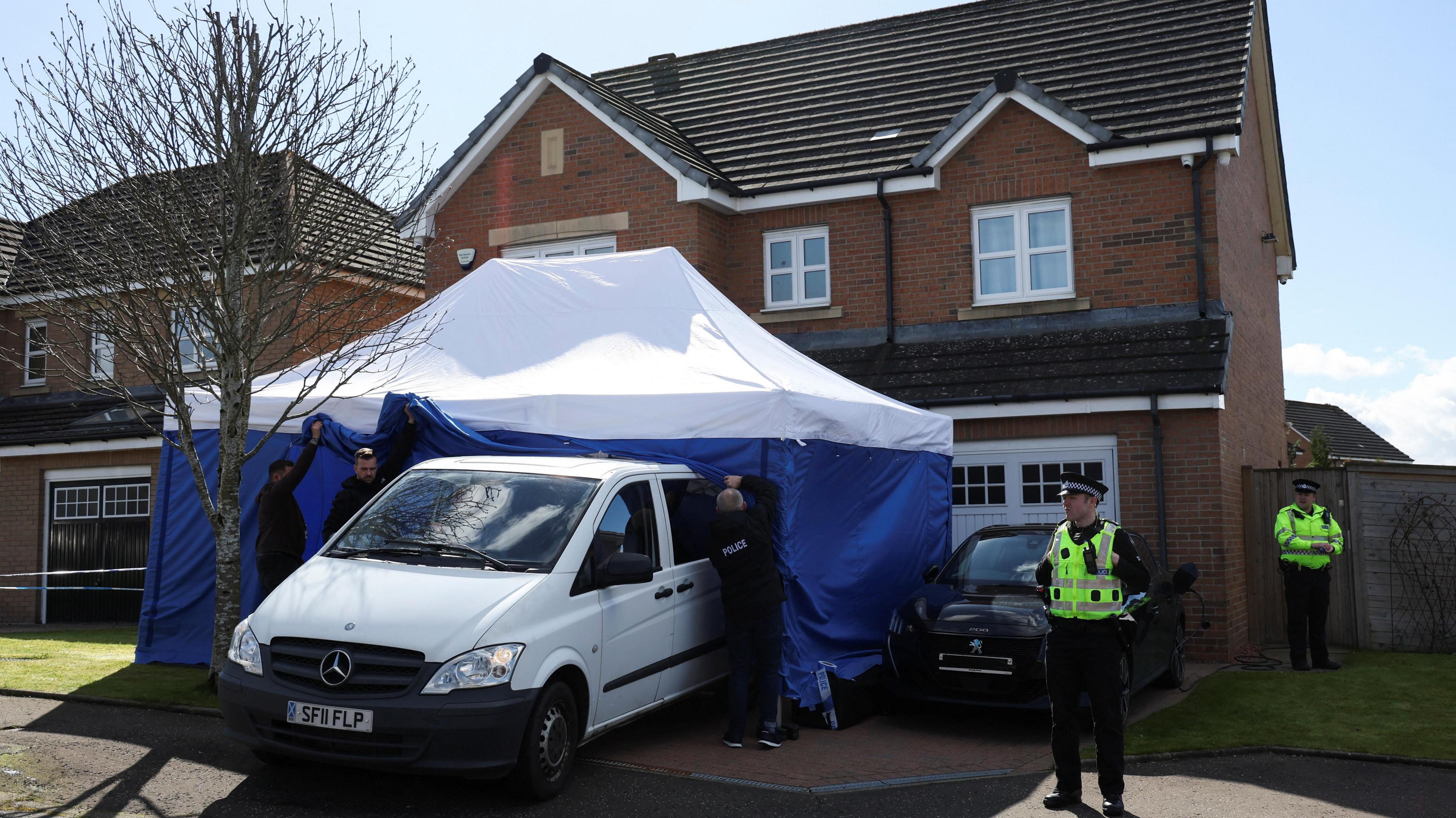 Peter Murrell's Glasgow detached house. A tent is outside the house with a van driving out of it. Police officers stand outside the house. 