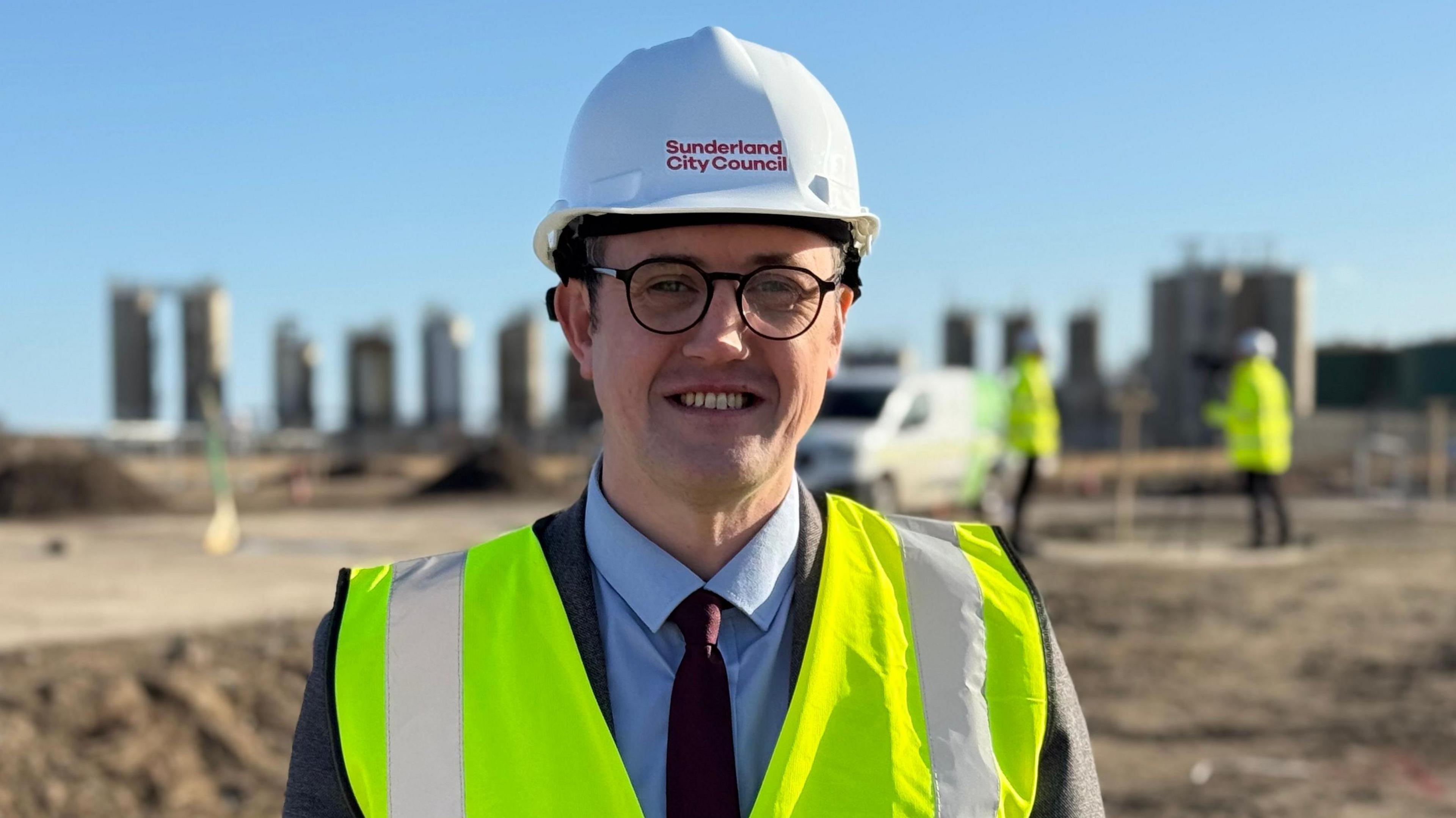 Michael Mordey stands on the construction site. He is wearing a yellow hi-vis jacket and a white hard-hat that reads: 'Sunderland City Council'