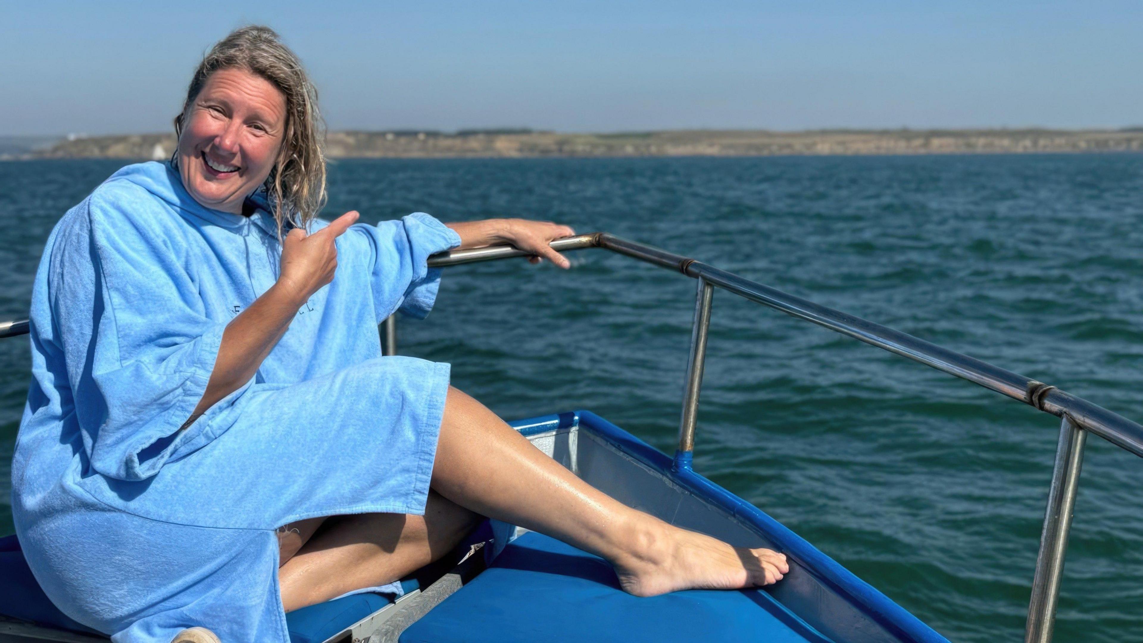 A woman in a blue robe sits on a boat pointing out to sea