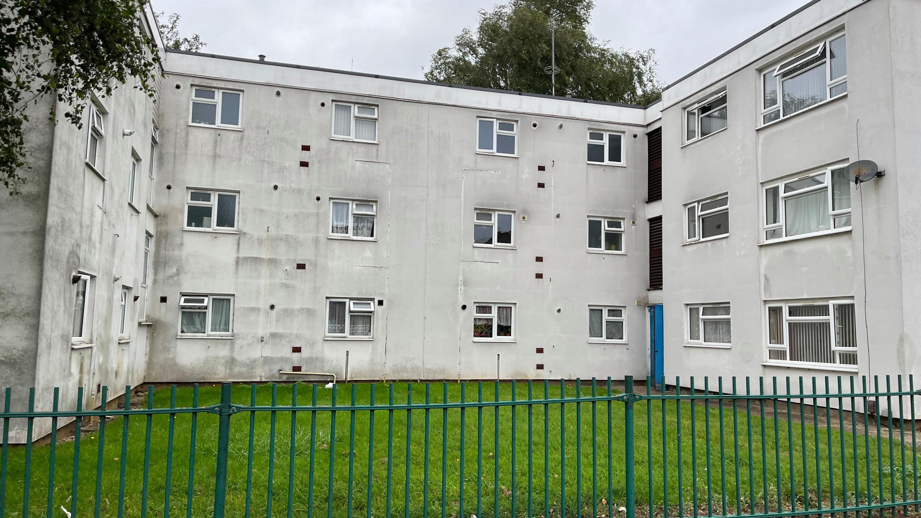 White block of flats at Alliston gardens with a green fence around the edge and grass in front