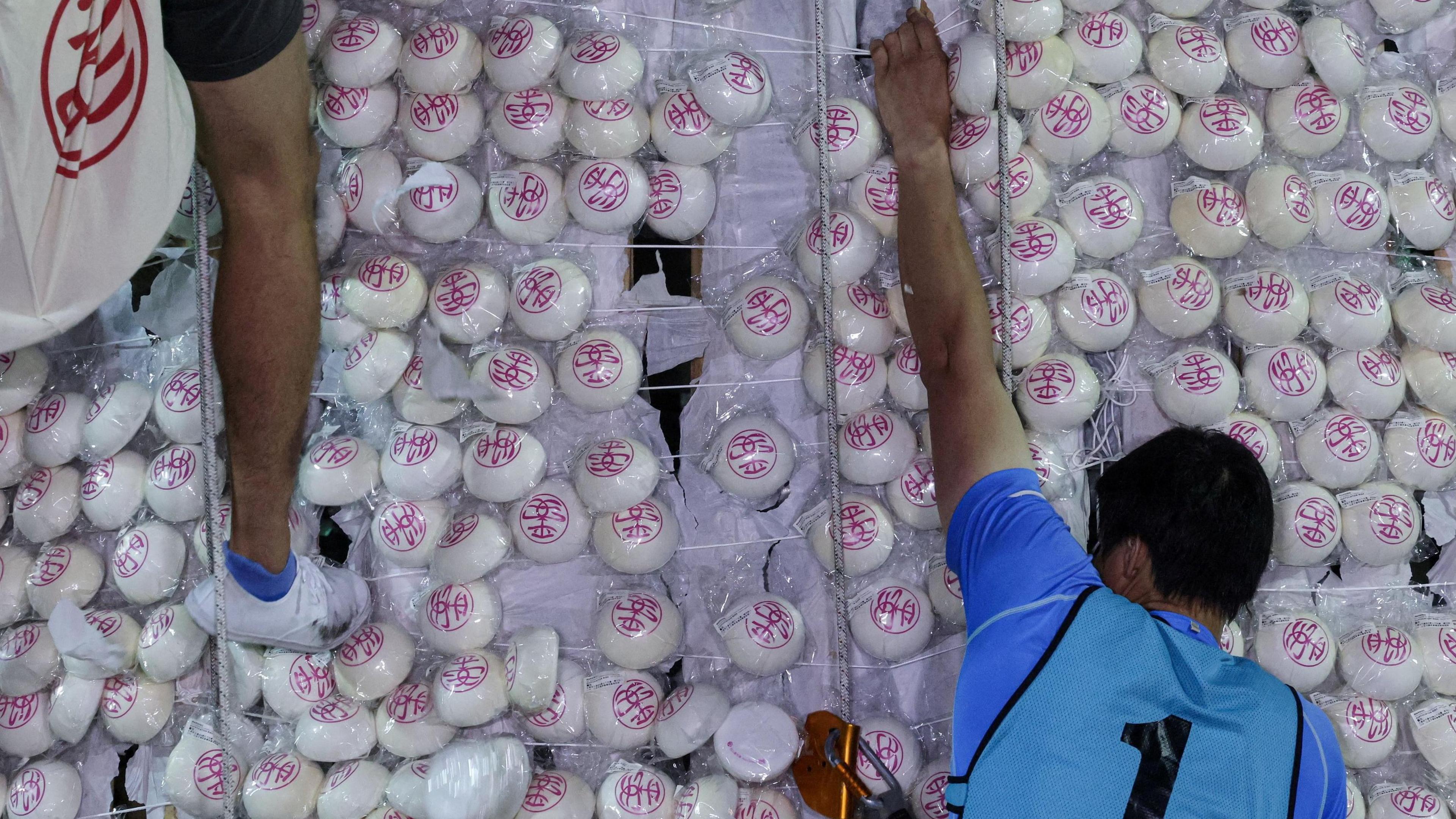 Man wearing a blue vest with number 1 written on it climbs a tower filled with buns.