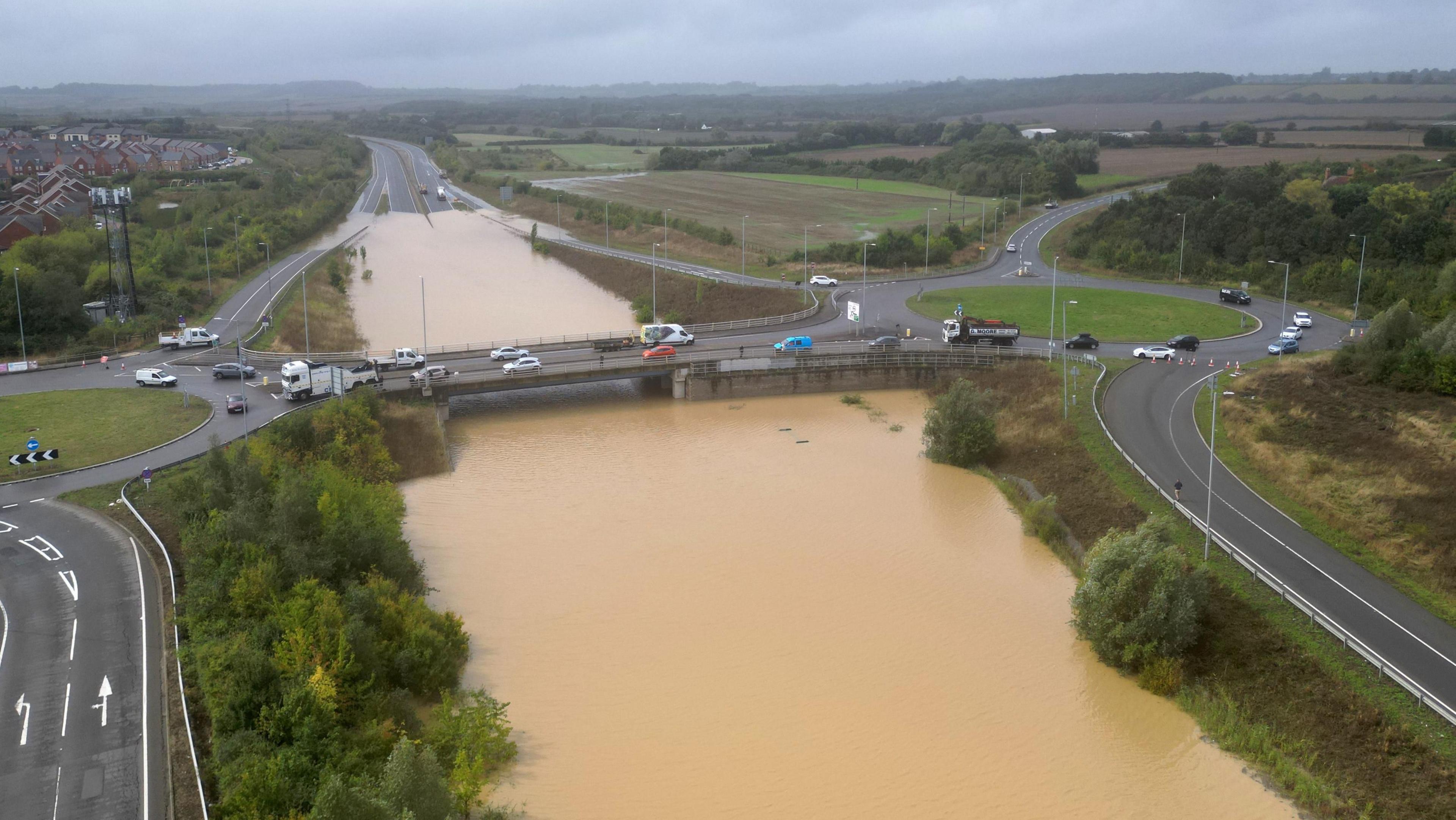 The open boot of a car is visible above a wide stretch of water on the A421 in Marston Moretain