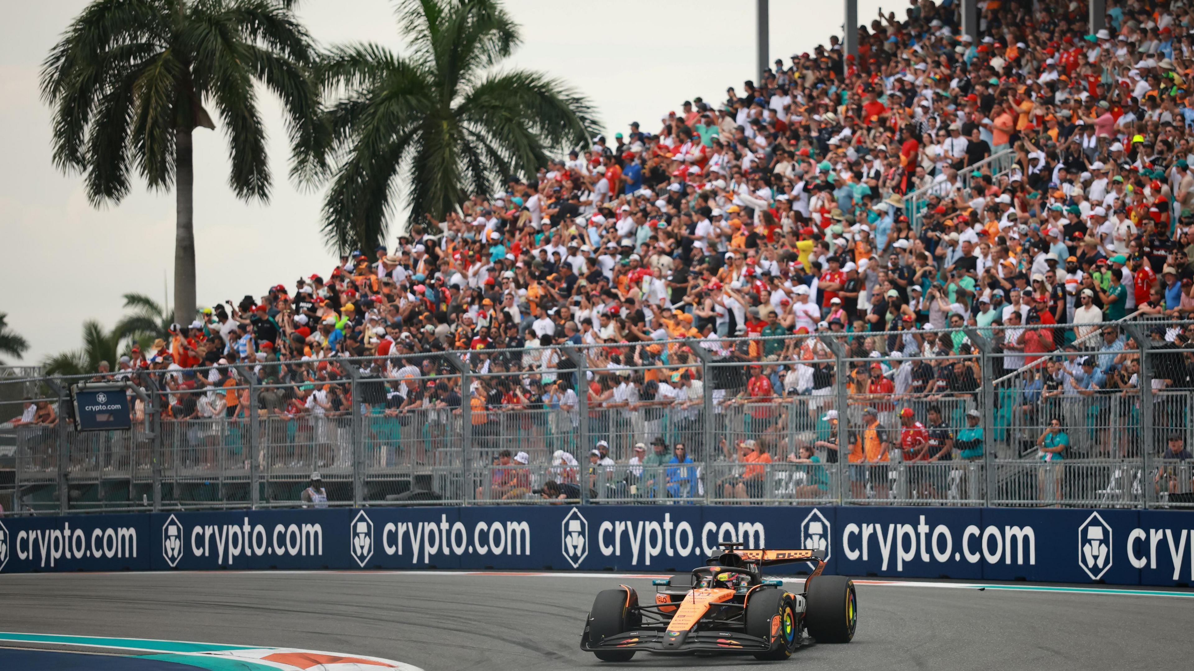 McLaren's Oscar Piastri turns into a right-hand corner during the 2025 Miami Grand Prix. A packed grandstand and two palm trees are in the background