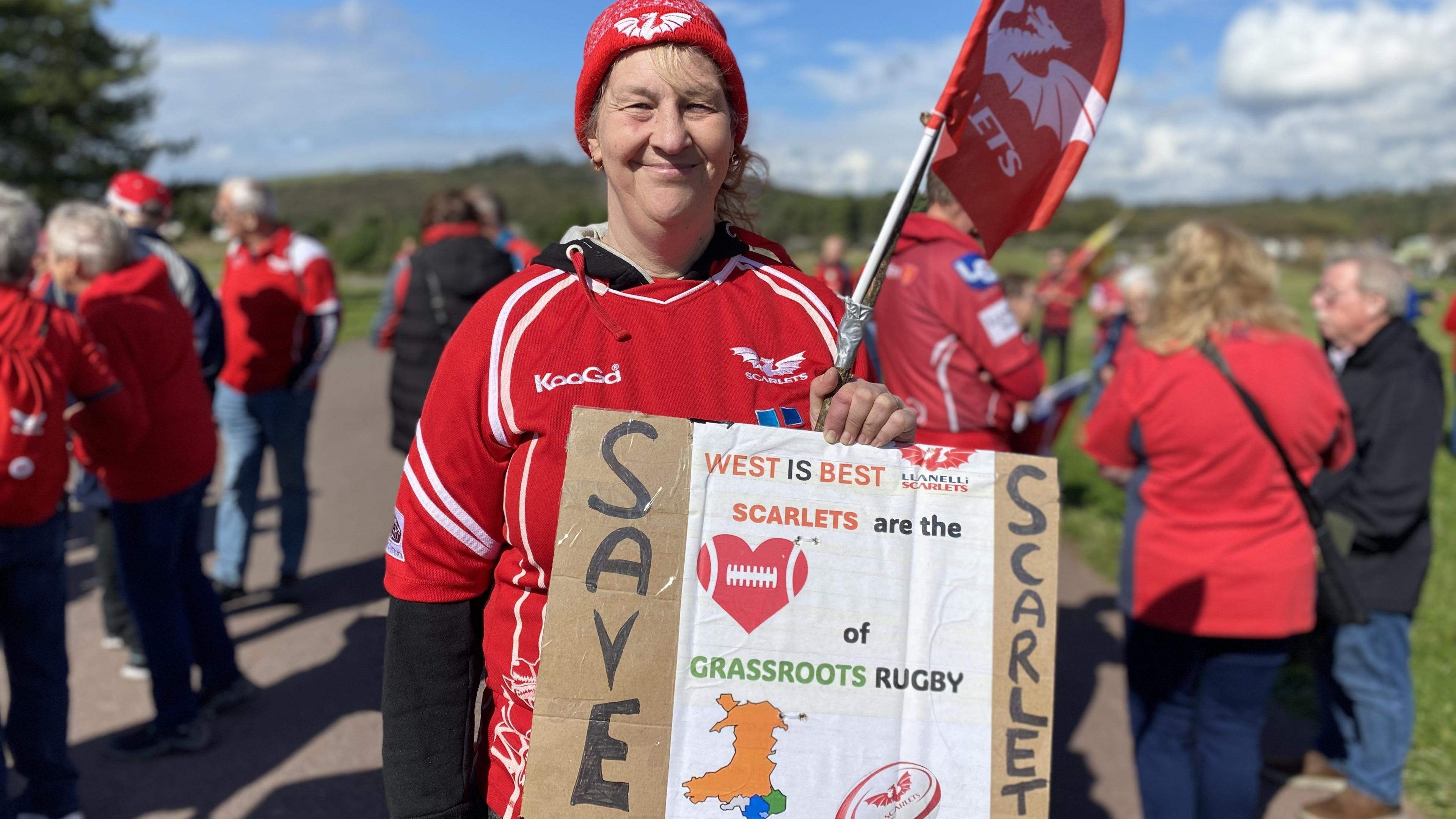 Helen Thomas marched in a scarlets jersey, flag and hat. she is holding a sign the says west if the best. Scarlets are the heart of grassroots rudby. 