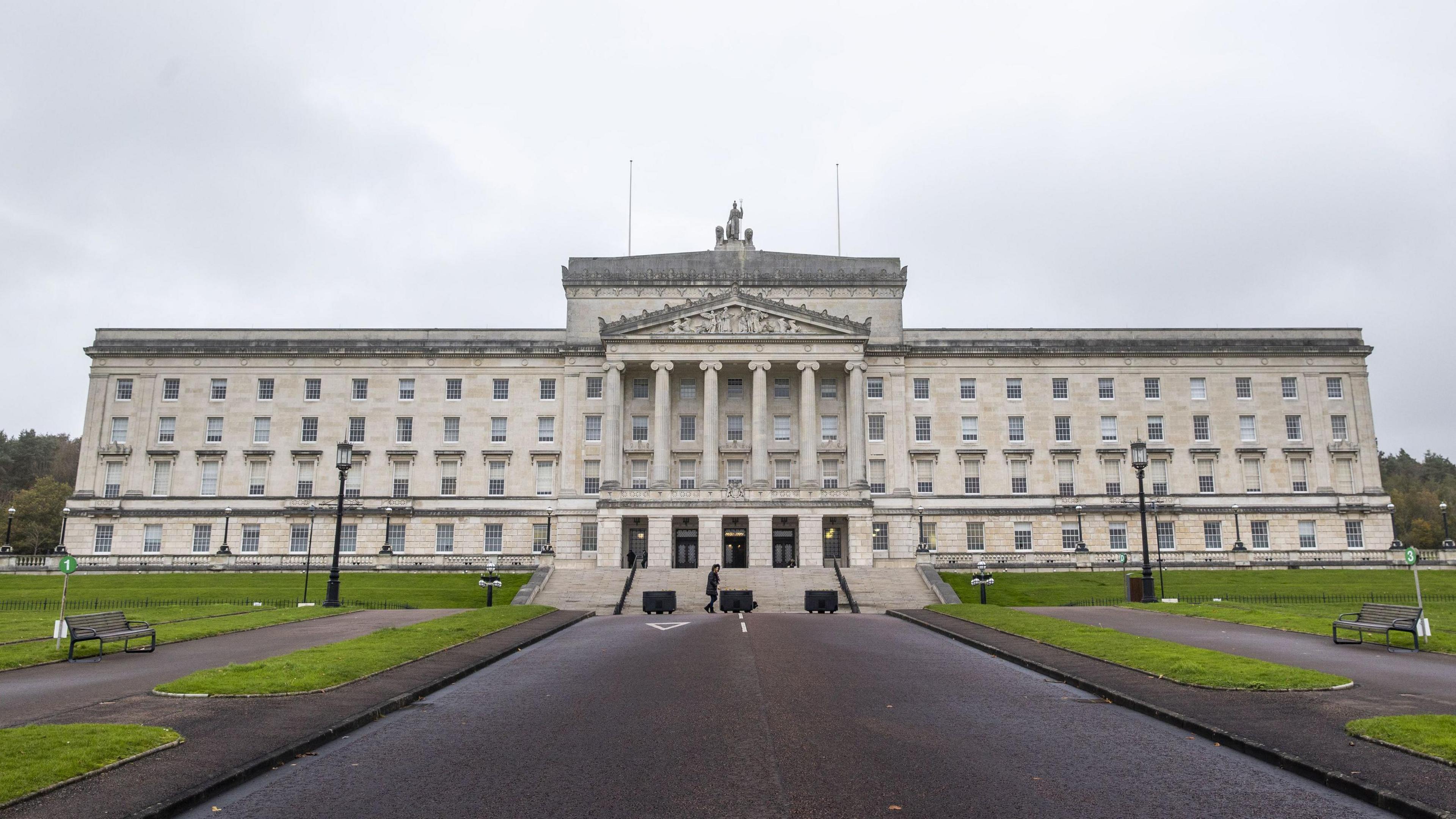 Parliament buildings at Stormont, a white Georgian style building pictured from the front, with the road leading up to it. 