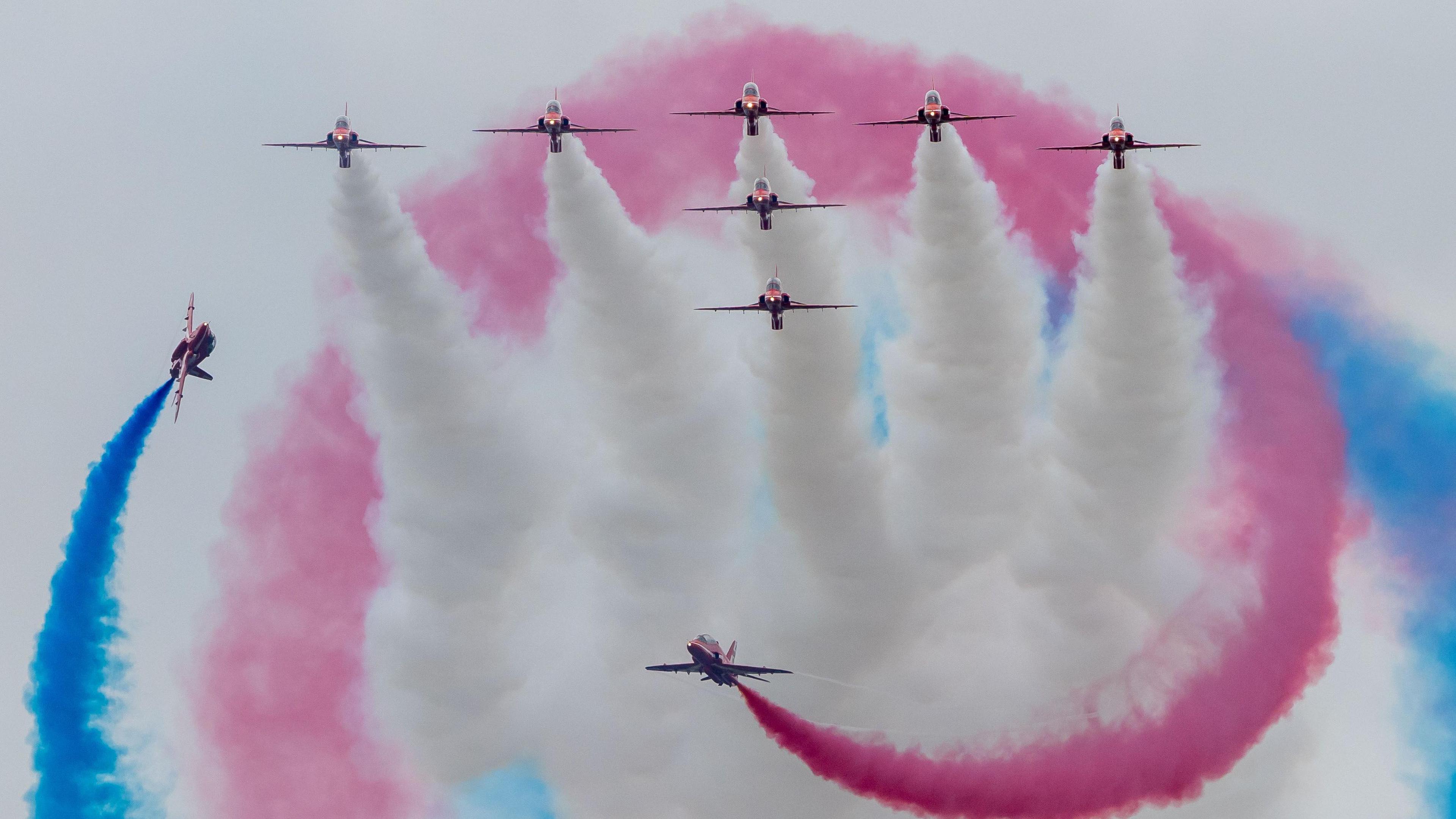 The Red Arrows perform an aerial routine, heading towards the camera, trailing red, blue and white smoke as they fly over the Royal International Air Tattoo at Fairford in Gloucestershire