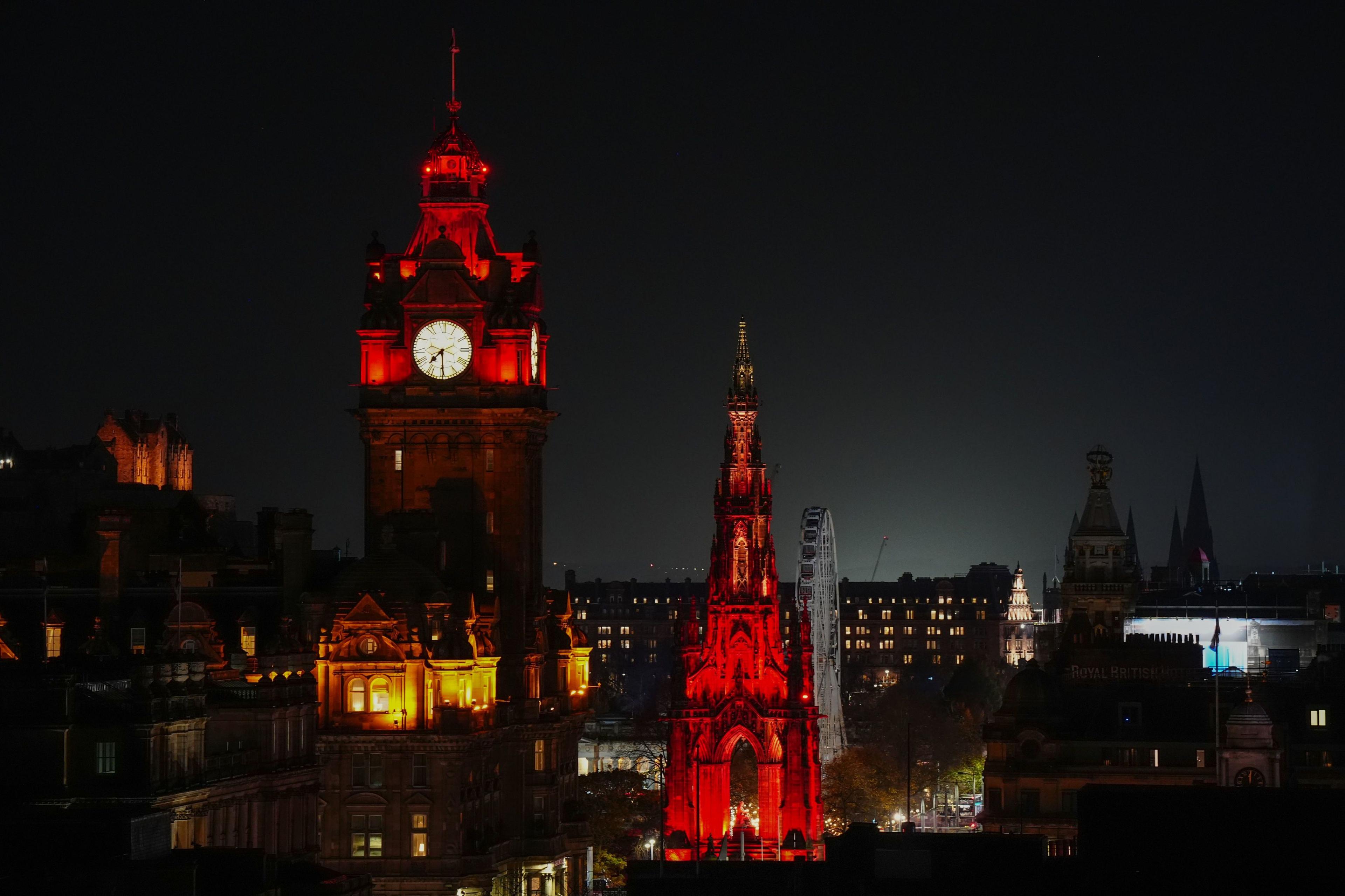 The Balmoral Clock and the Scott Monument in Edinburgh are illuminated in red light against a dark sky in support of the 2025 PoppyScotland Appeal.