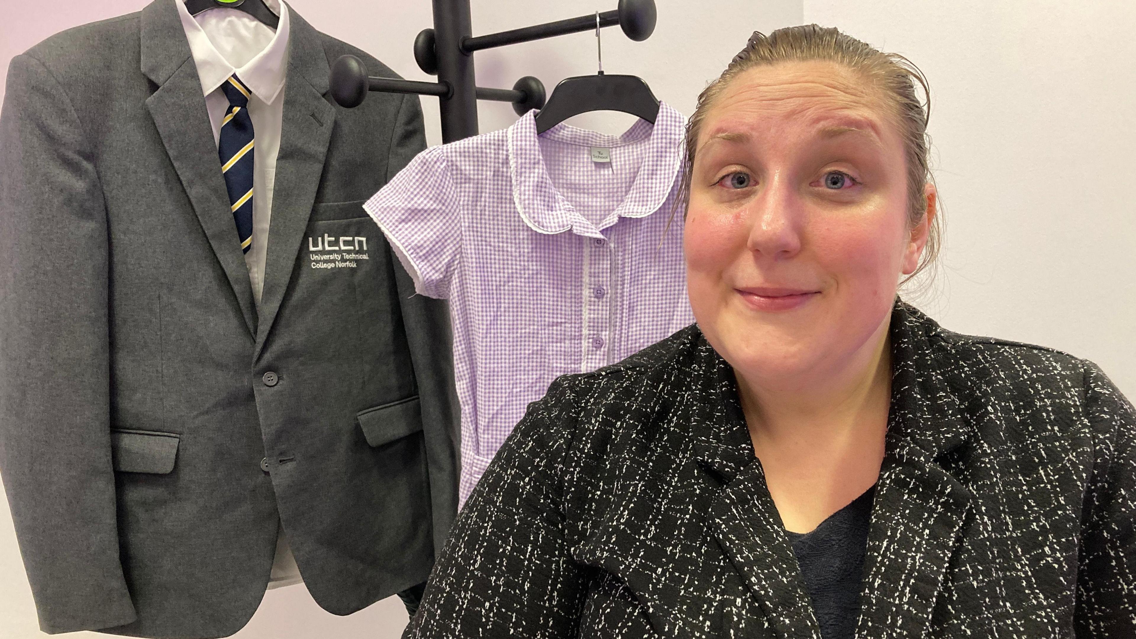 Marketing manager Gemma Hyde, who is wearing a black-and-white checked jacket, smiles as she stands in front of donated school uniform.