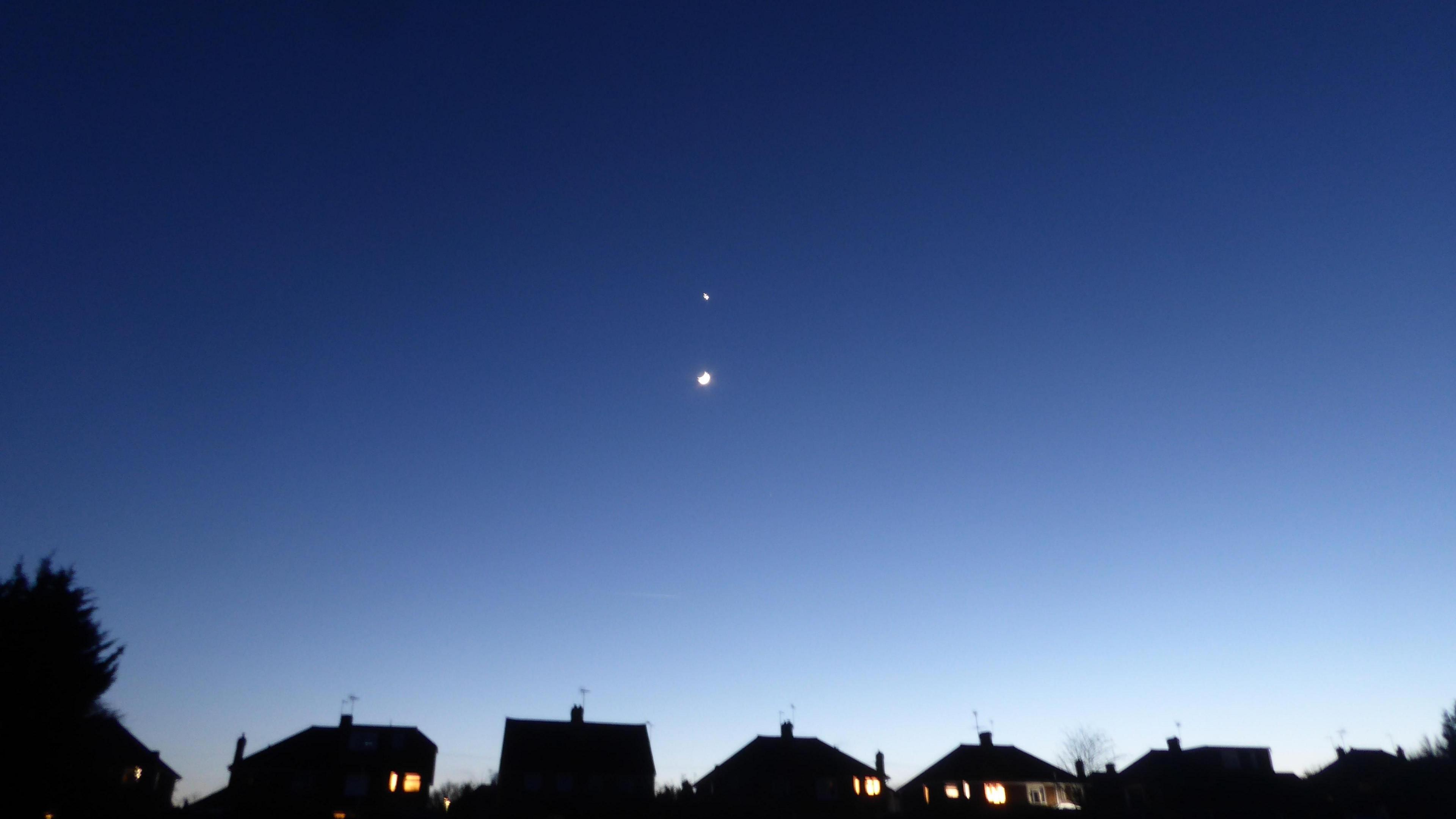 The Moon and Venus in the night sky, with the silhouettes of houses below.