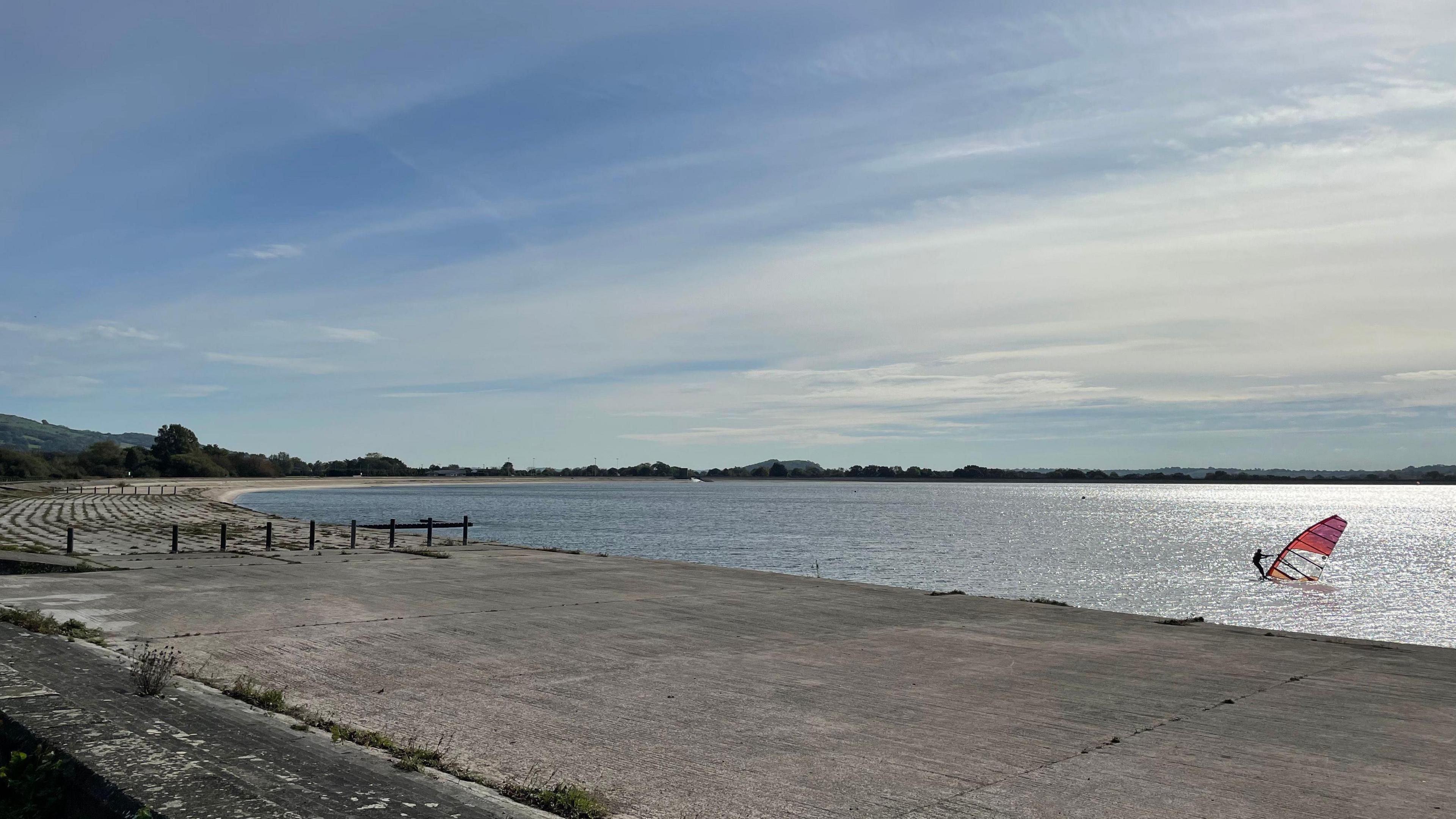 a windsurfer on a reservoir on a sunny day with the concrete banks of the water exposed