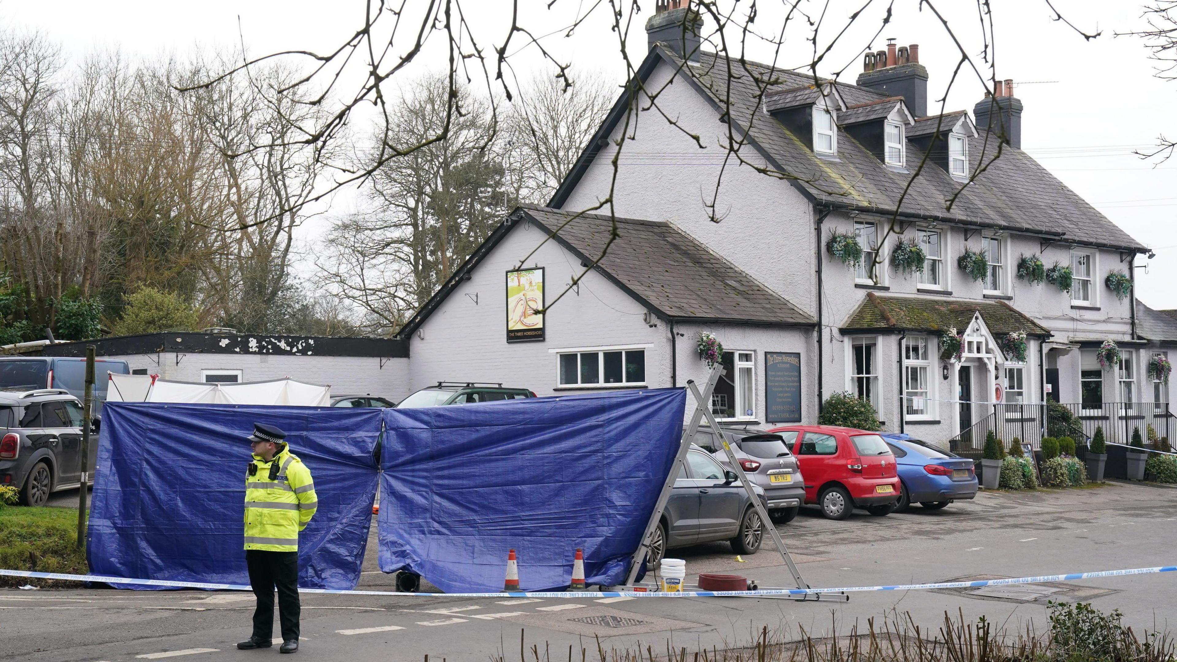 A police officer stands outside of a pub that is cordoned off with police tape. 