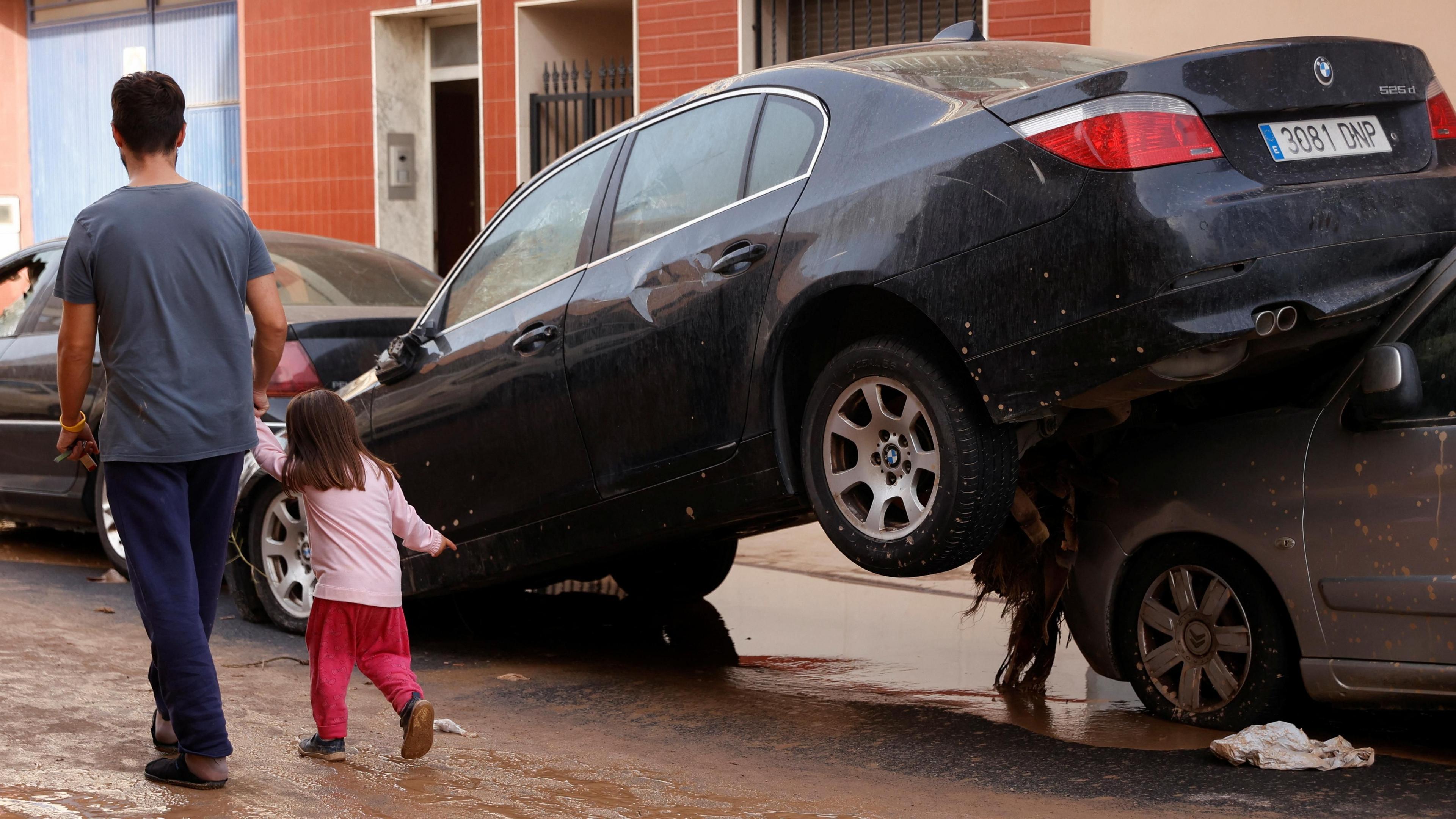 Man and young girl walk on a street next to damaged cars after torrential rains caused flooding in Guadassuar, Valencia region, Spain, 30 October 2024