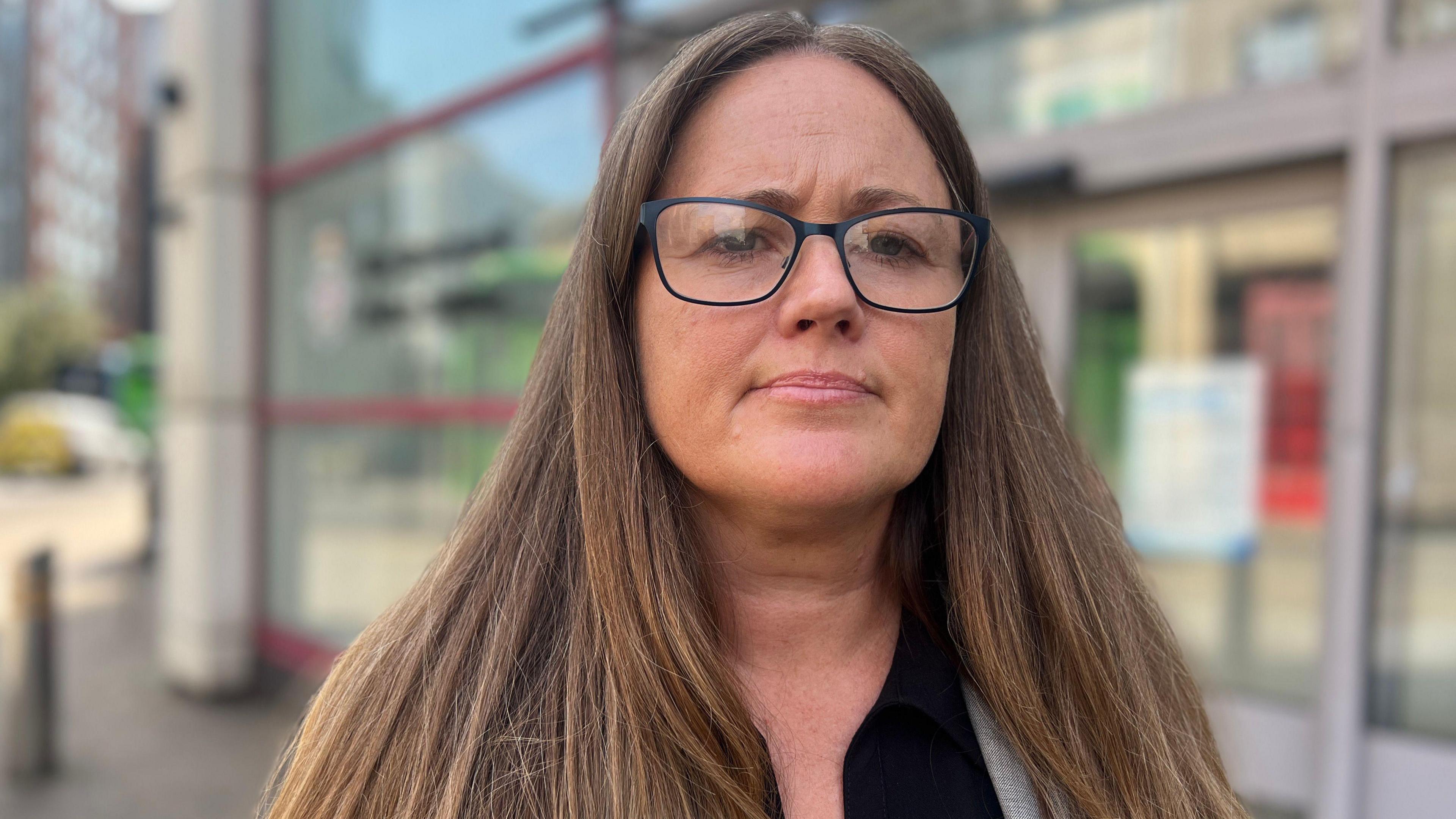 A head and shoulders shot of Det Sgt Sarah Bowden. She has long straight brown hair and is wearing glasses, looking at the camera with a thoughtful expression.