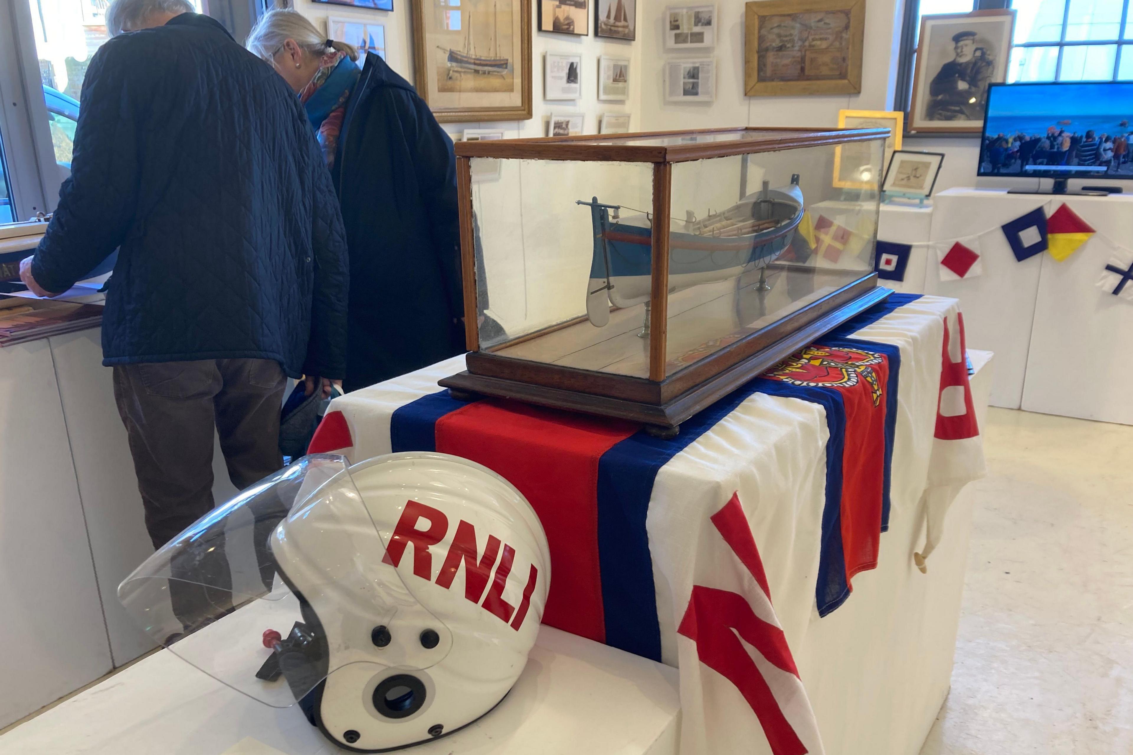 An old white RNLI helmet next to a display case with a model of an old lifeboat inside 