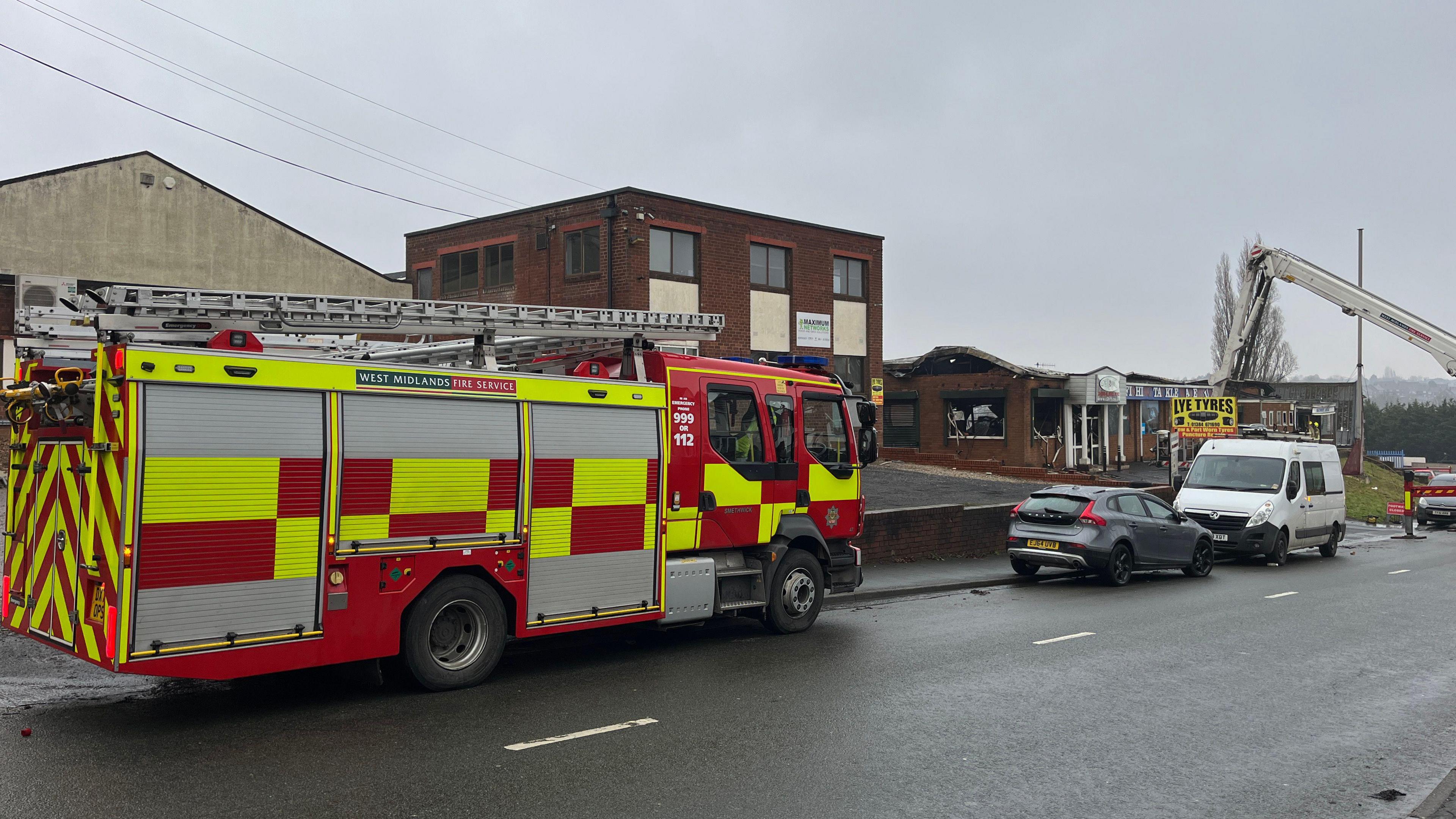 A fire engine is parked on the road near a commercial building with fire damage.