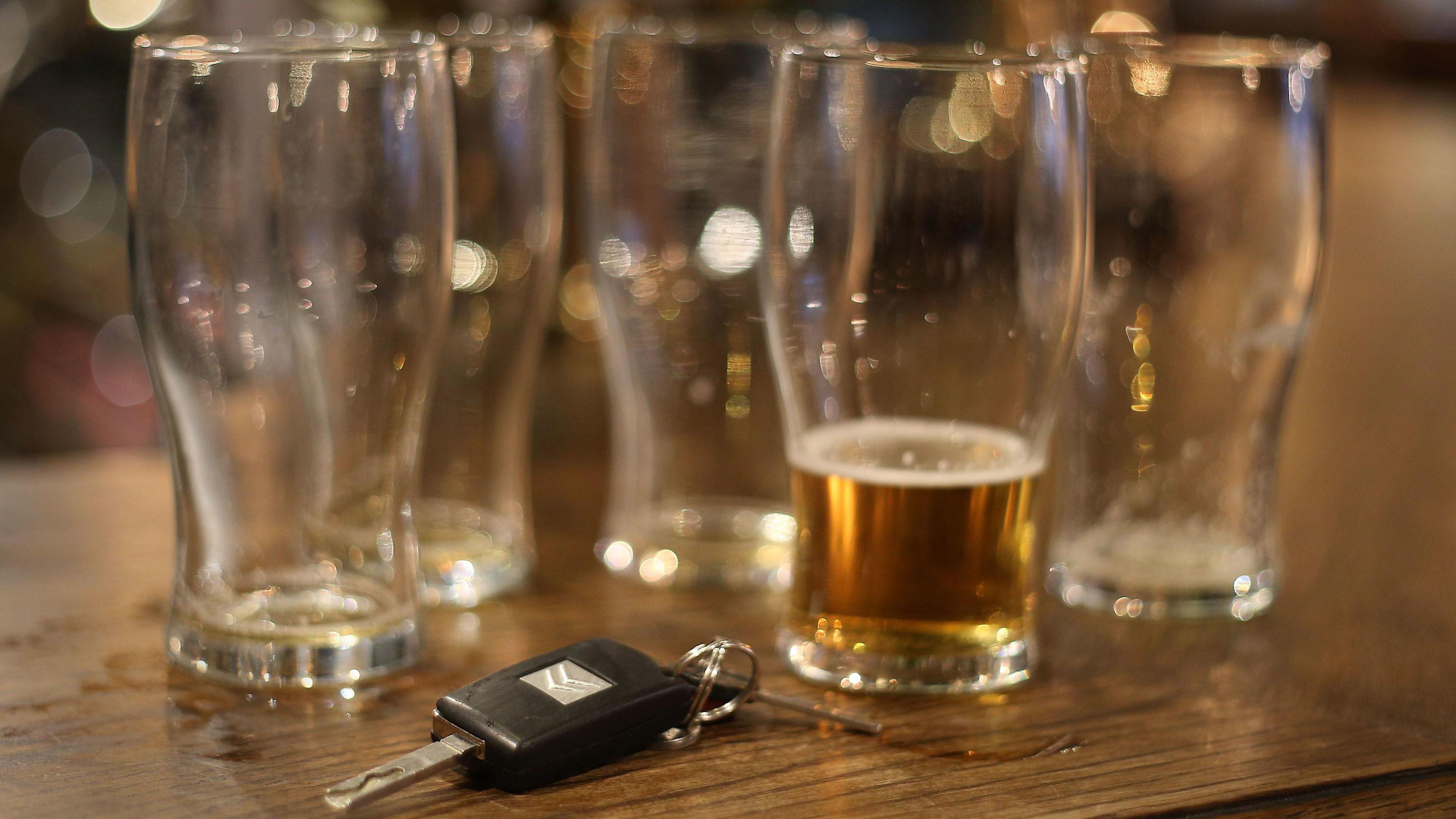 Four empty pint glasses next to one glass with a small amount of lager left in it. Some car keys are beside the glasses on a wooden table in a pub.