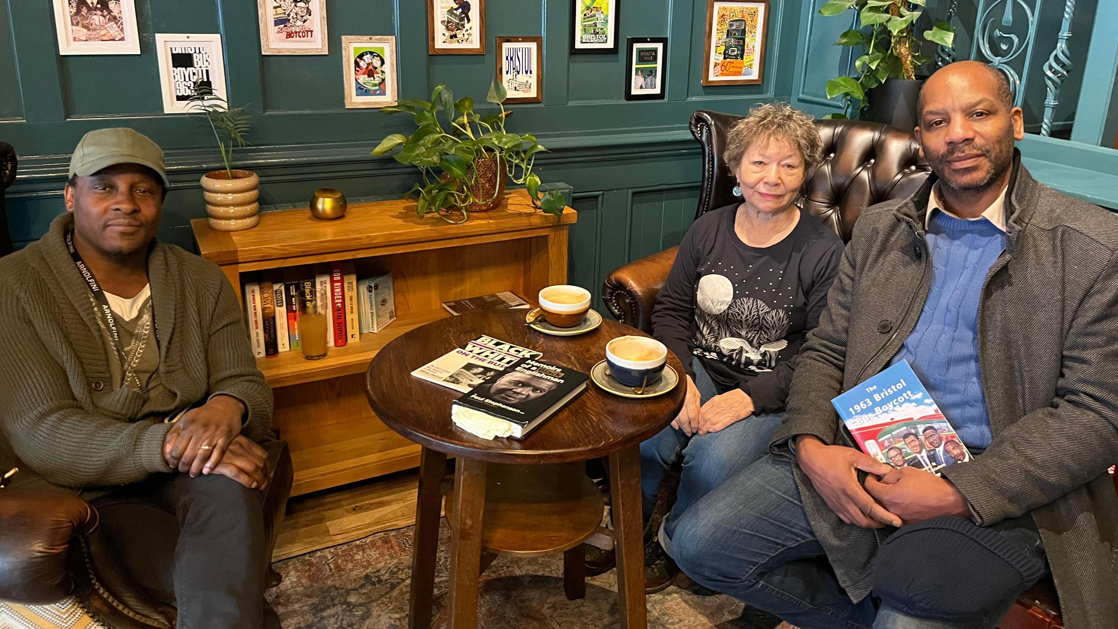 Julian, Lilleith and Rob sit in a corner of The Bay Horse on a mixture of sofas and wooden chairs. A copy of Dr Stephenson's book is on a coffee table, which also has a couple of large coffee on it. They are all looking at the camera. 