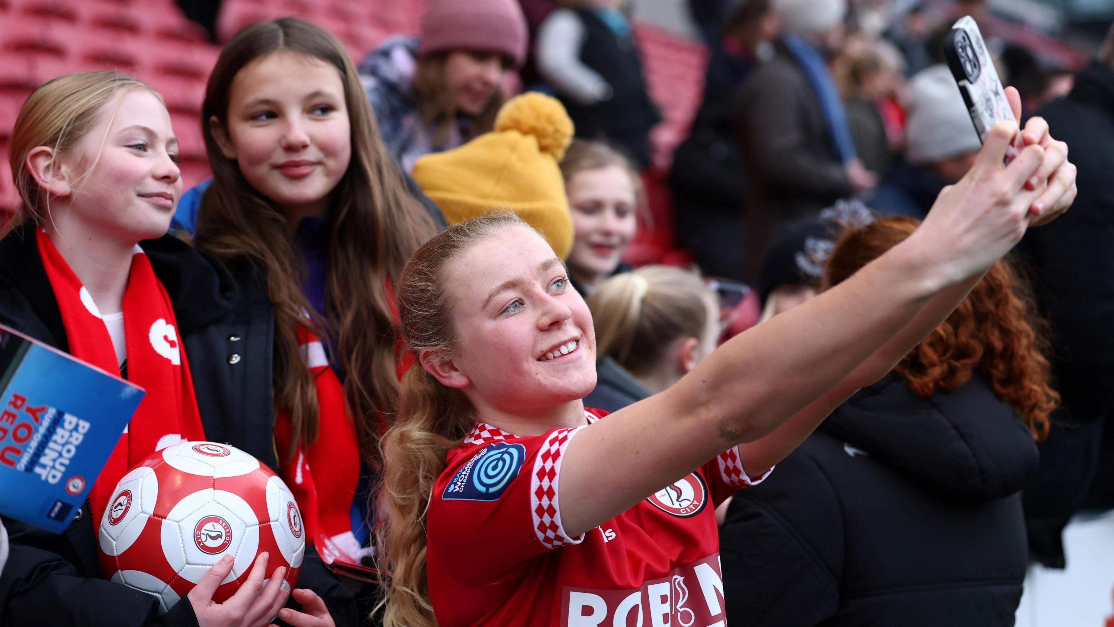 Bristol City Women's FC player Mari Ward stretches out her arms so she can take a selfie with two young female fans at Ashton Gate after the game with Southampton.