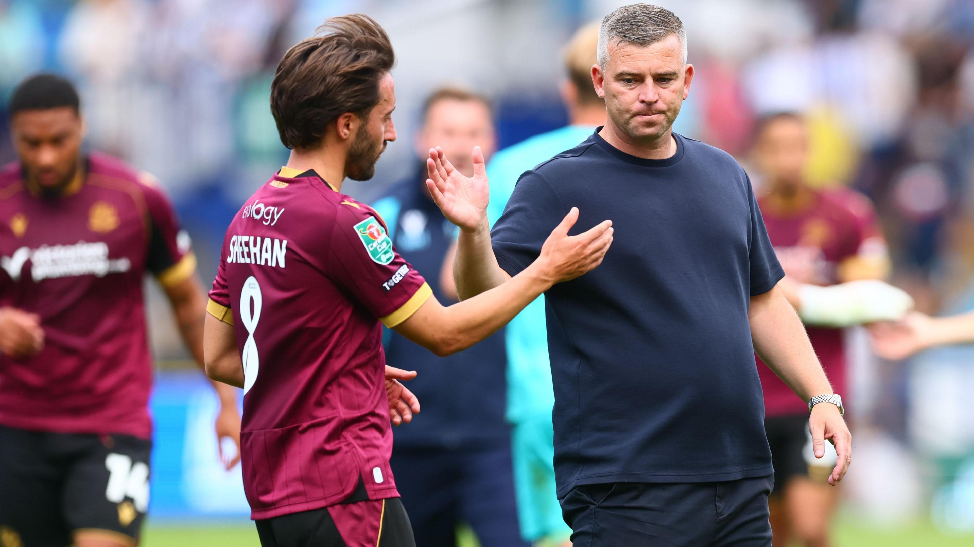 Steven Schumacher, wearing a navy blue t-shirt, claps hands with midfielder Josh Sheehan, who is wearing Bolton's maroon away kit, after the 1-0 defeat to Sheffield Wednesday in the EFL Cup at Hillsborough