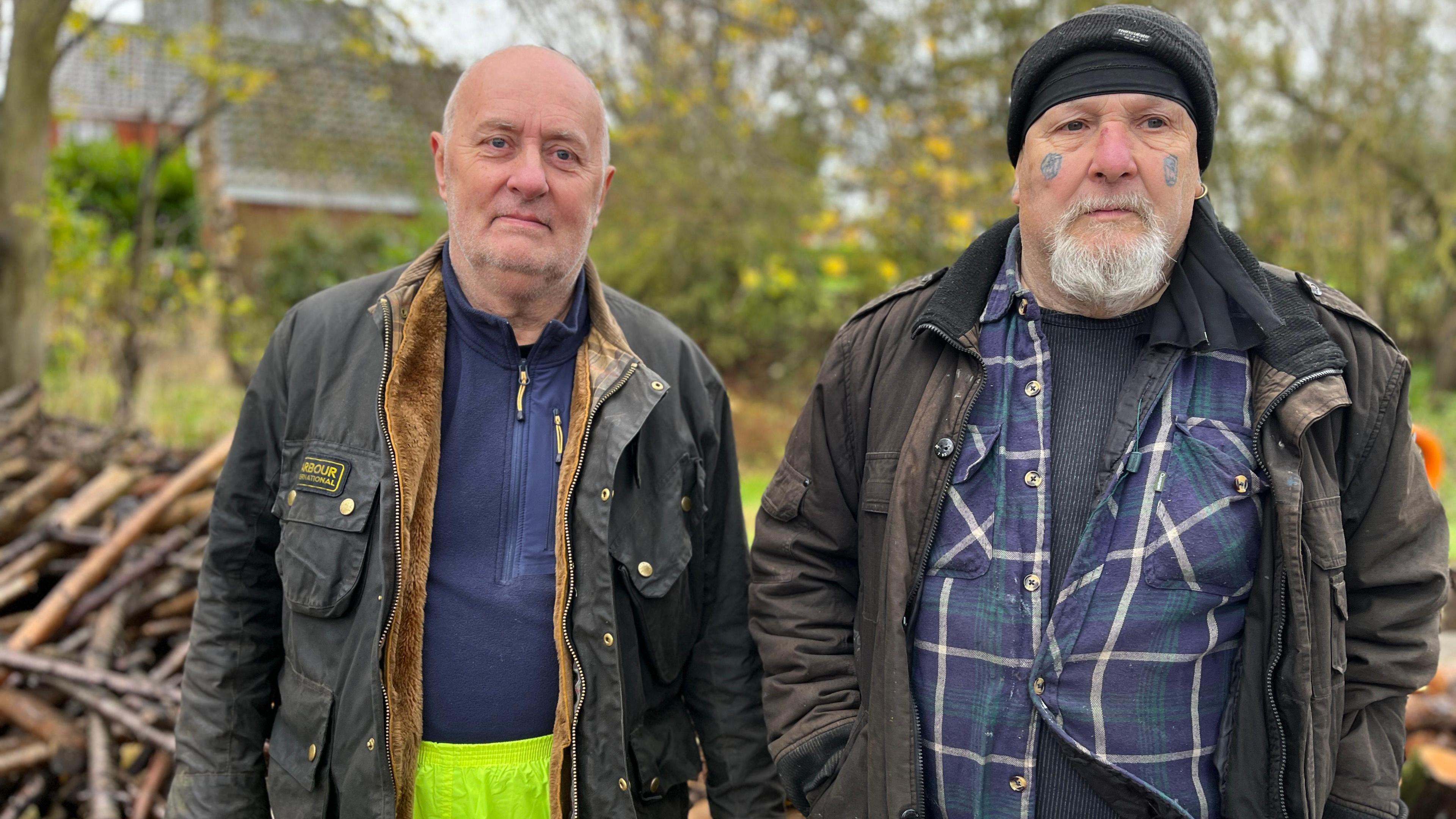 Colin Cripps and Stephen St Claire standing in front of a wood pile.