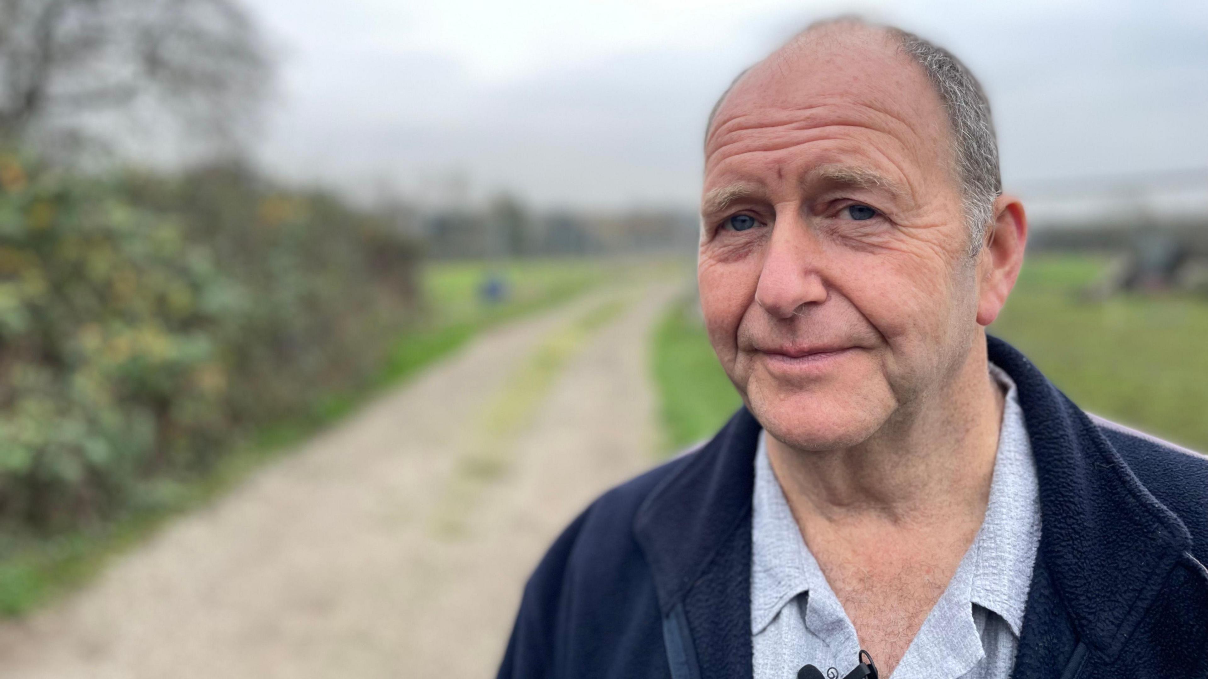 Man in grey shirt and blue jacket in front of a footpath