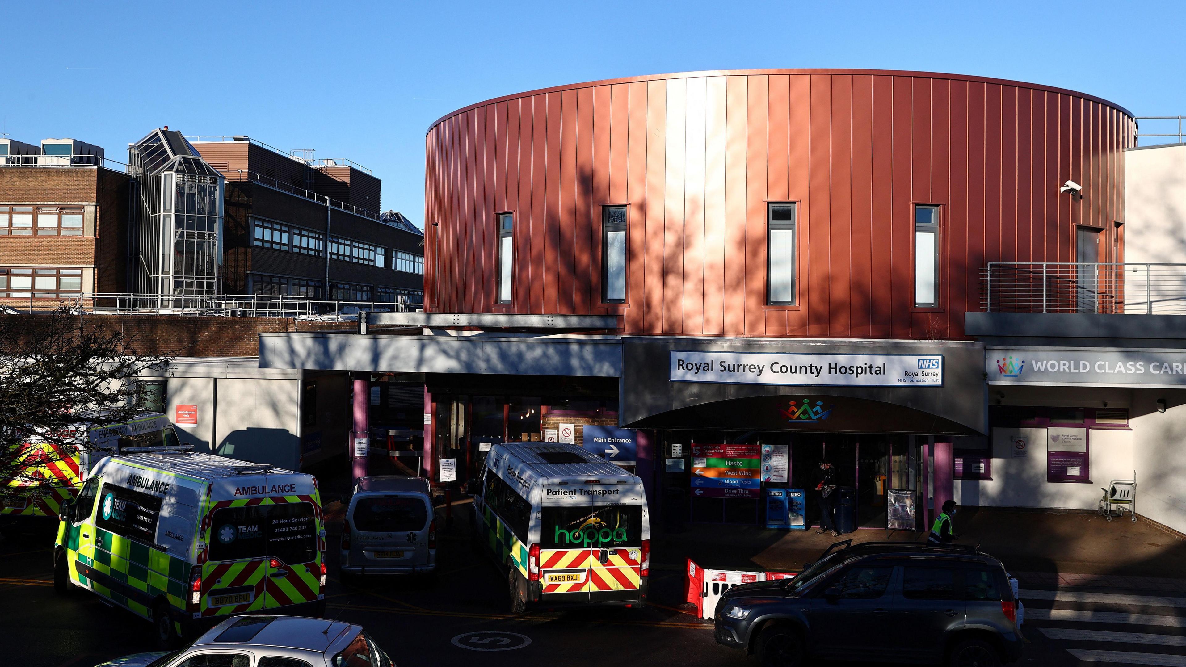 The exterior of the Royal Surrey County Hospital, with the sign clearly prominent and several ambulances parked in front of it.