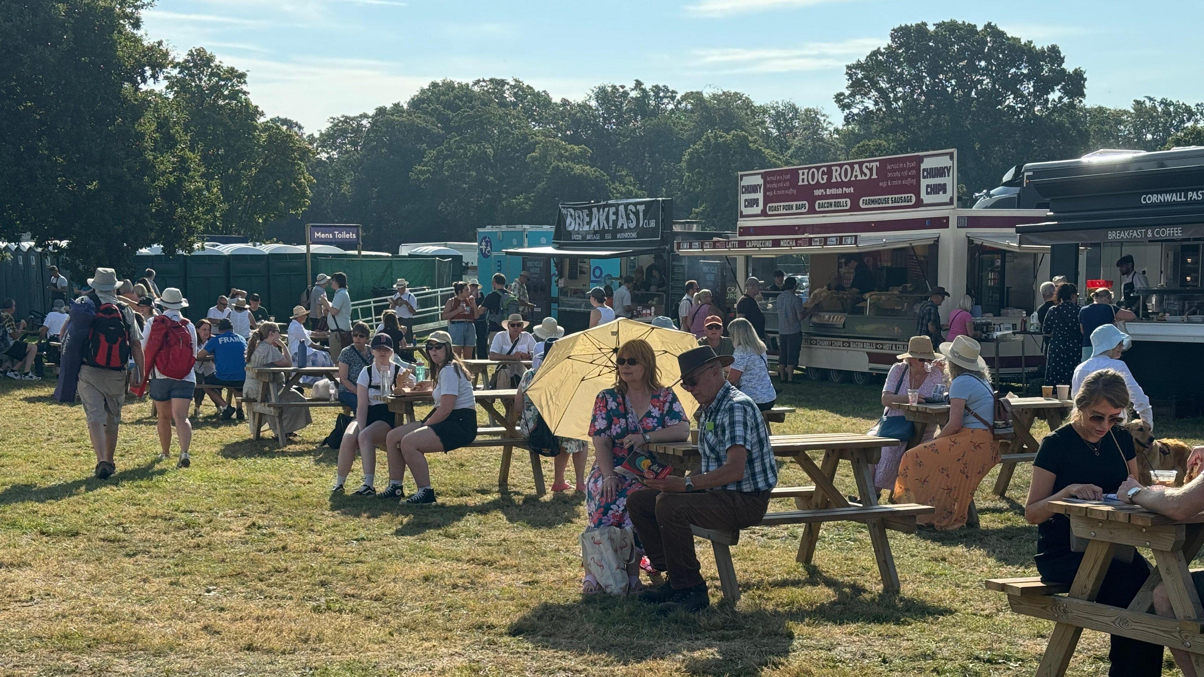 People sat on wooden benches in front of an array of different food vendors.