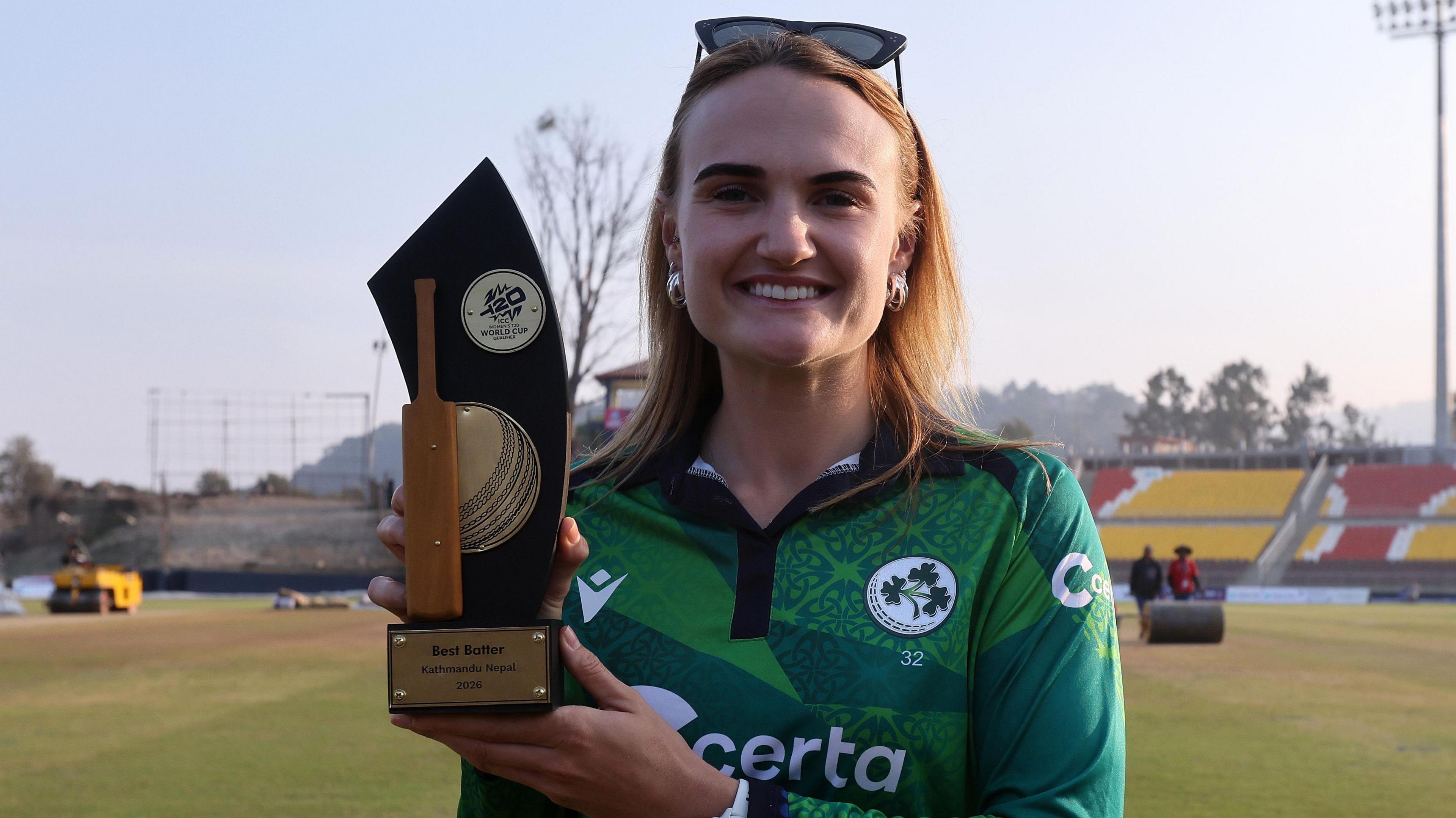 Gaby Lewis in an empty stadium holding the trophy for the tournament's best batter