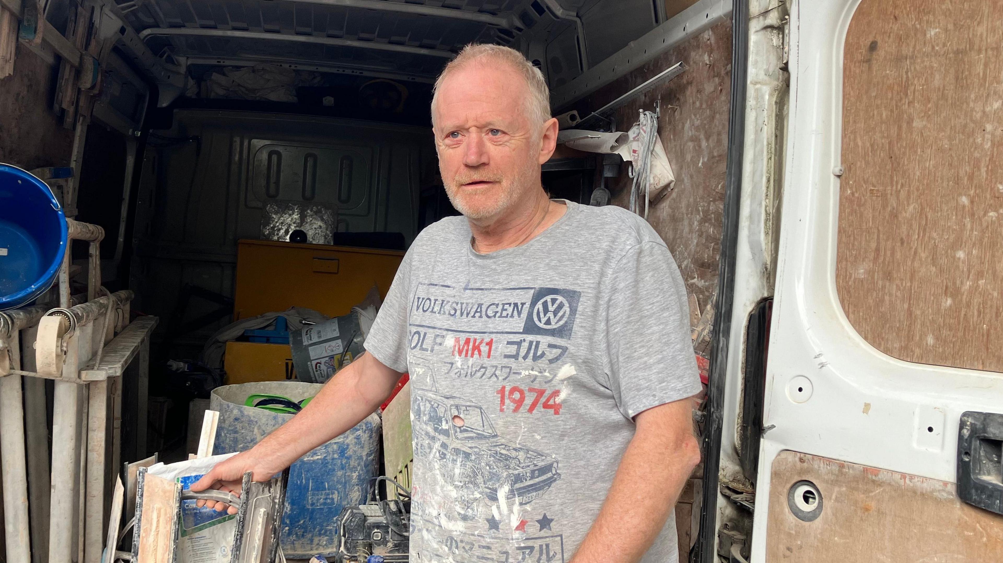 Paul Dougherty  is standing at the back door of his work van. He is wearing a grey T-shirt and is looking slightly to the left of the camera.