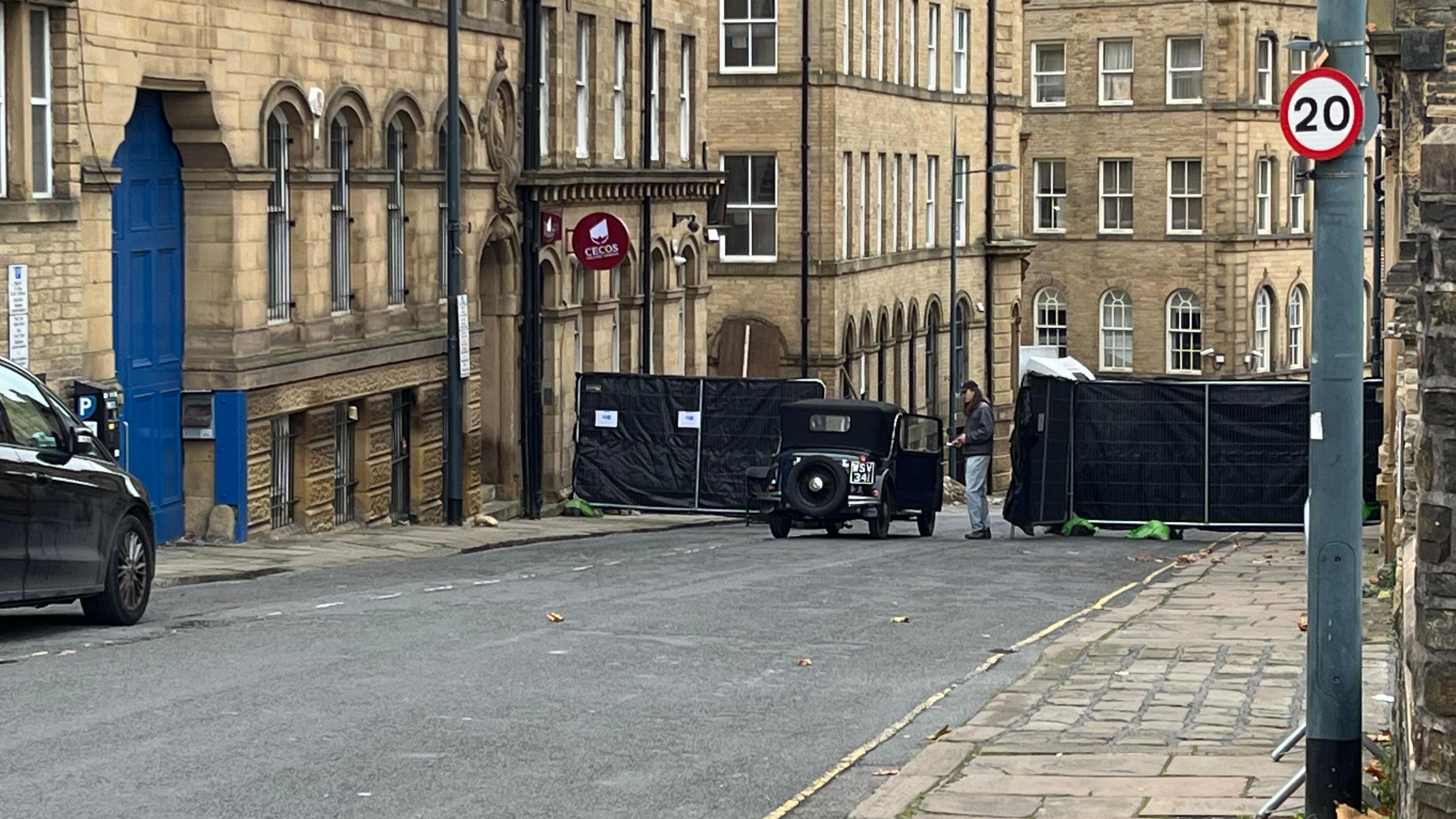 Car on historic Bradford street in front of blacked out gate